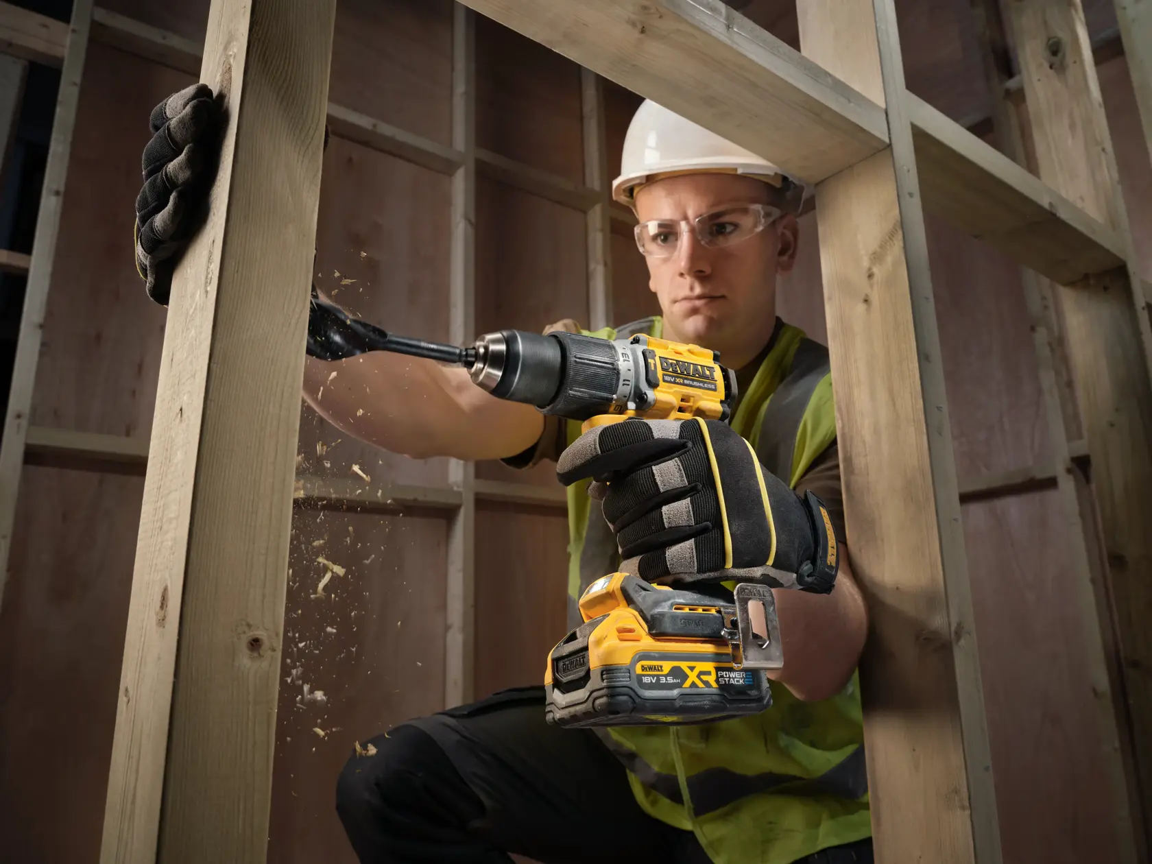 Trabajador perfora viga de madera con taladro DEWALT inalámbrico, usando guantes y equipo de seguridad.