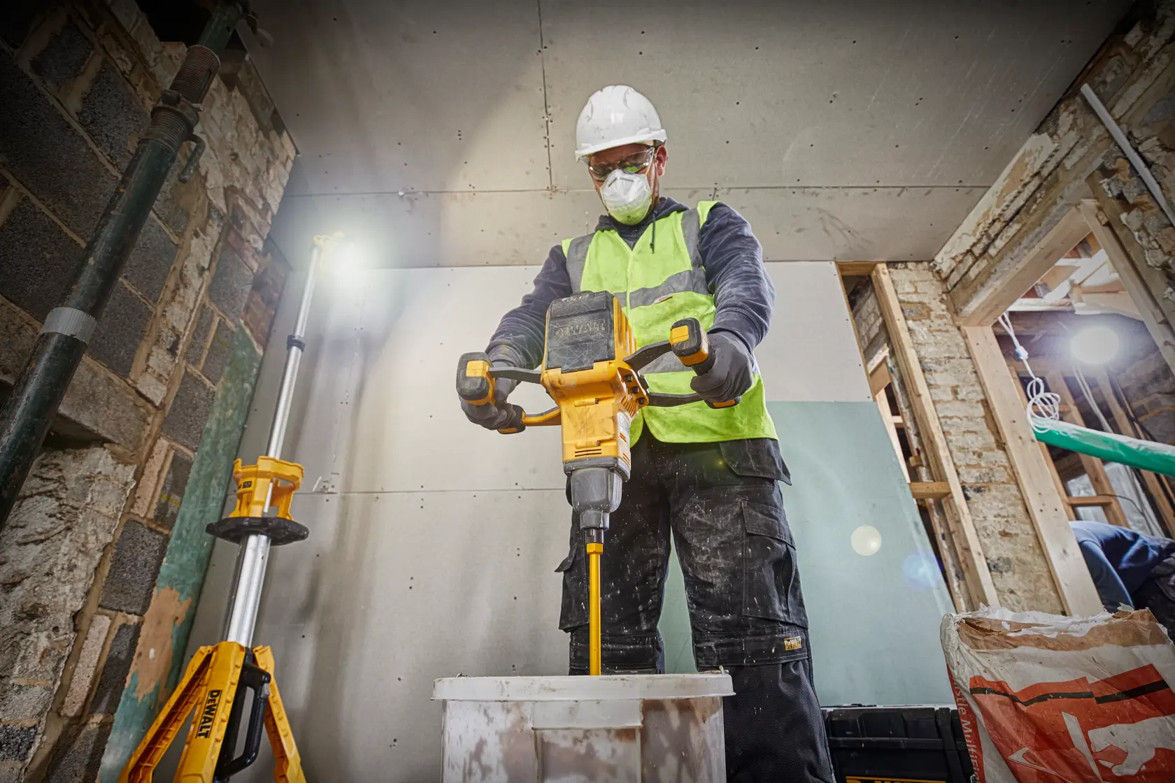 Arbeiter mischt Material mit DEWALT Werkzeug, trägt Sicherheitsausrüstung und Warnweste.