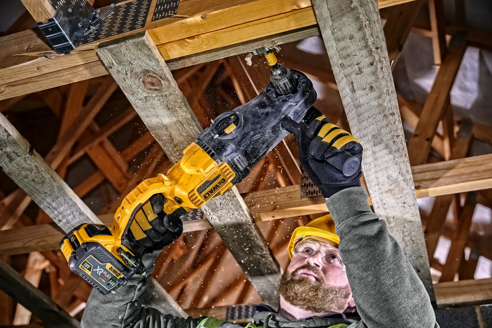 Eine Person verwendet einen DEWALT DCD470N Akkubohrer, um ein Loch in einen Holzbalken bei Bauarbeiten zu bohren. Der Arbeiter trägt Schutzhandschuhe und einen Sicherheitshelm.