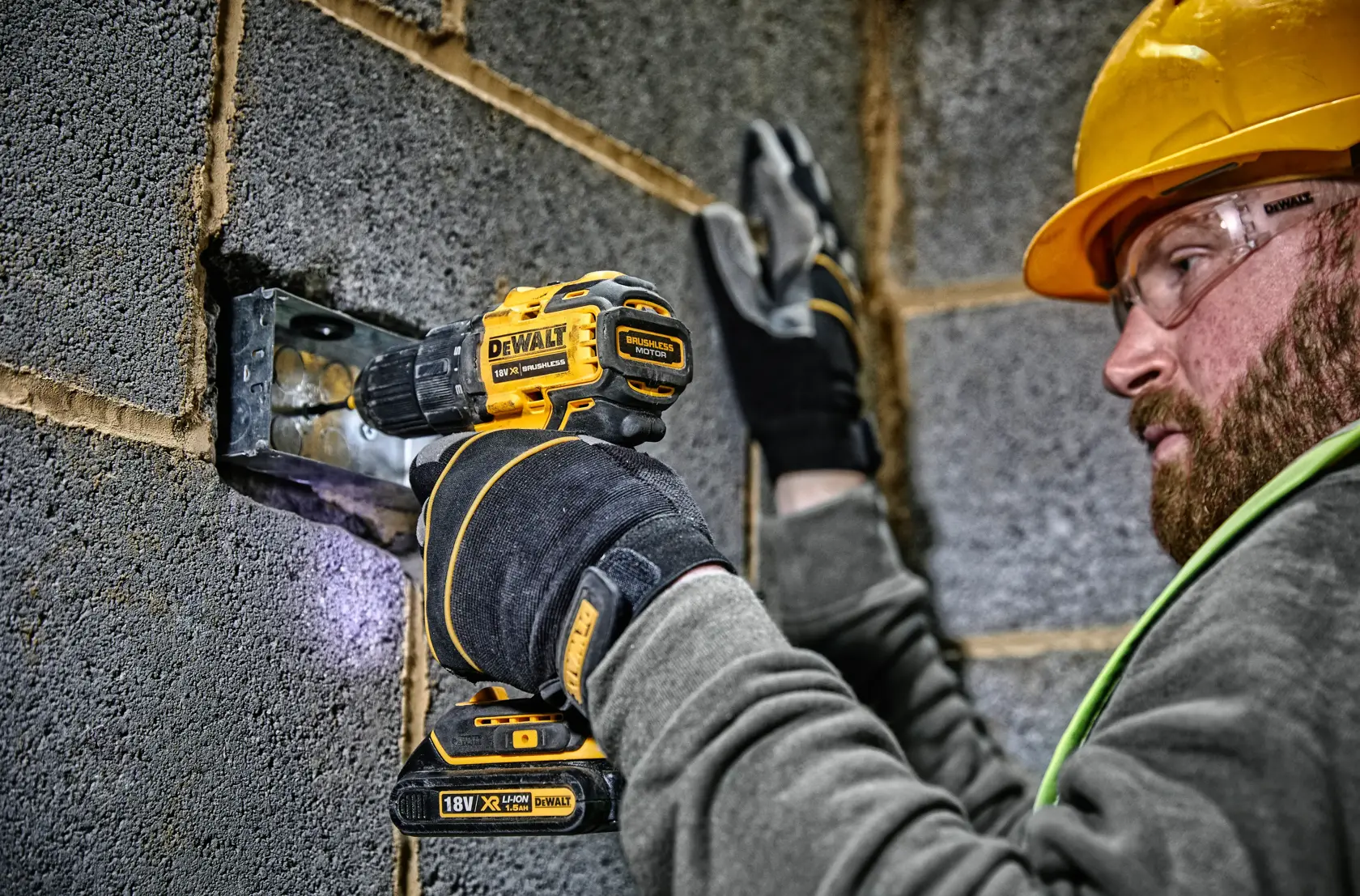 Une personne portant des gants et un casque de sécurité utilise une perceuse-visseuse sans fil DEWALT 18V (modèle DCD708) pour travailler sur un élément métallique dans un mur en parpaings.