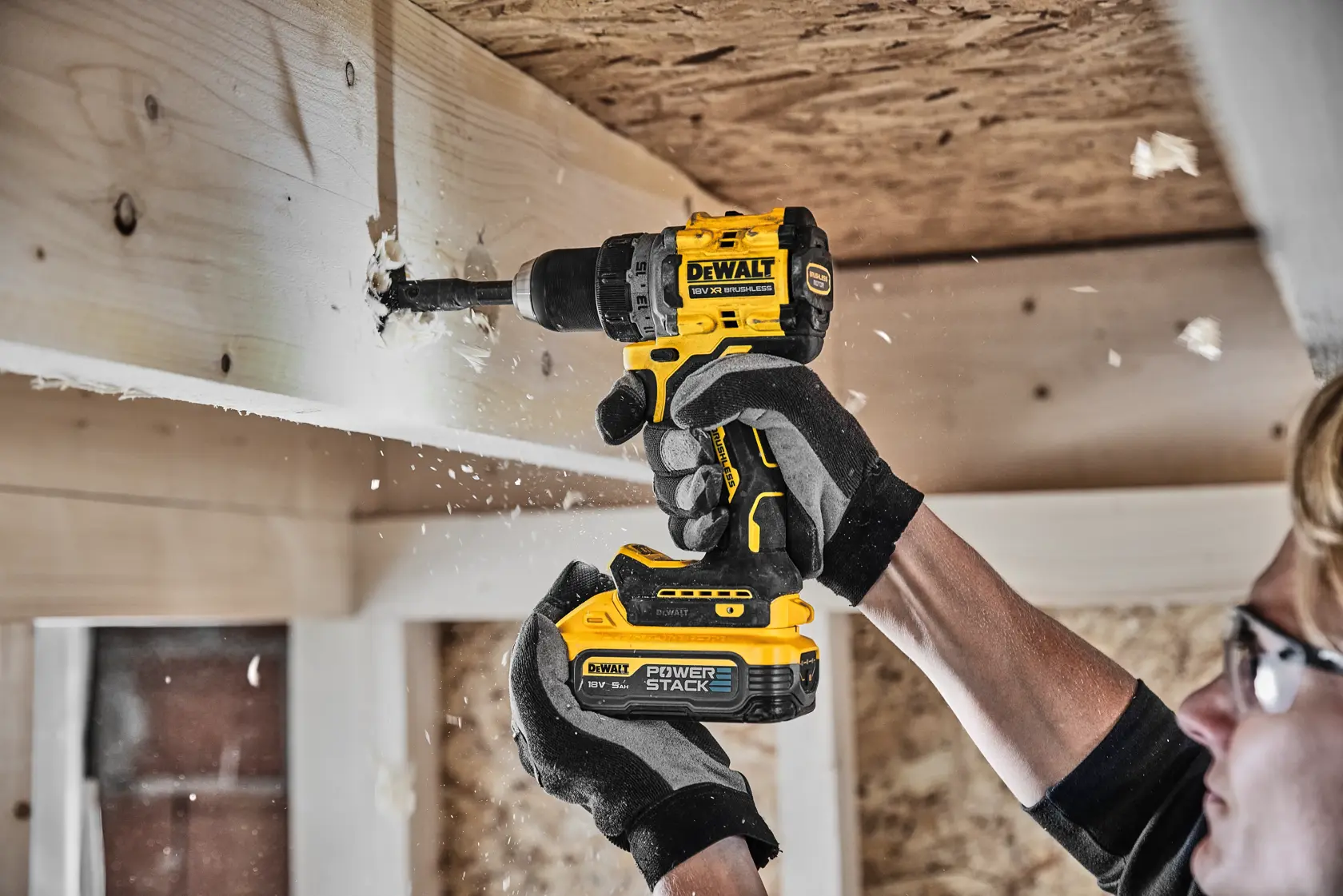Persona perfora viga de madera con taladro DEWALT, usando guantes y gafas de seguridad.