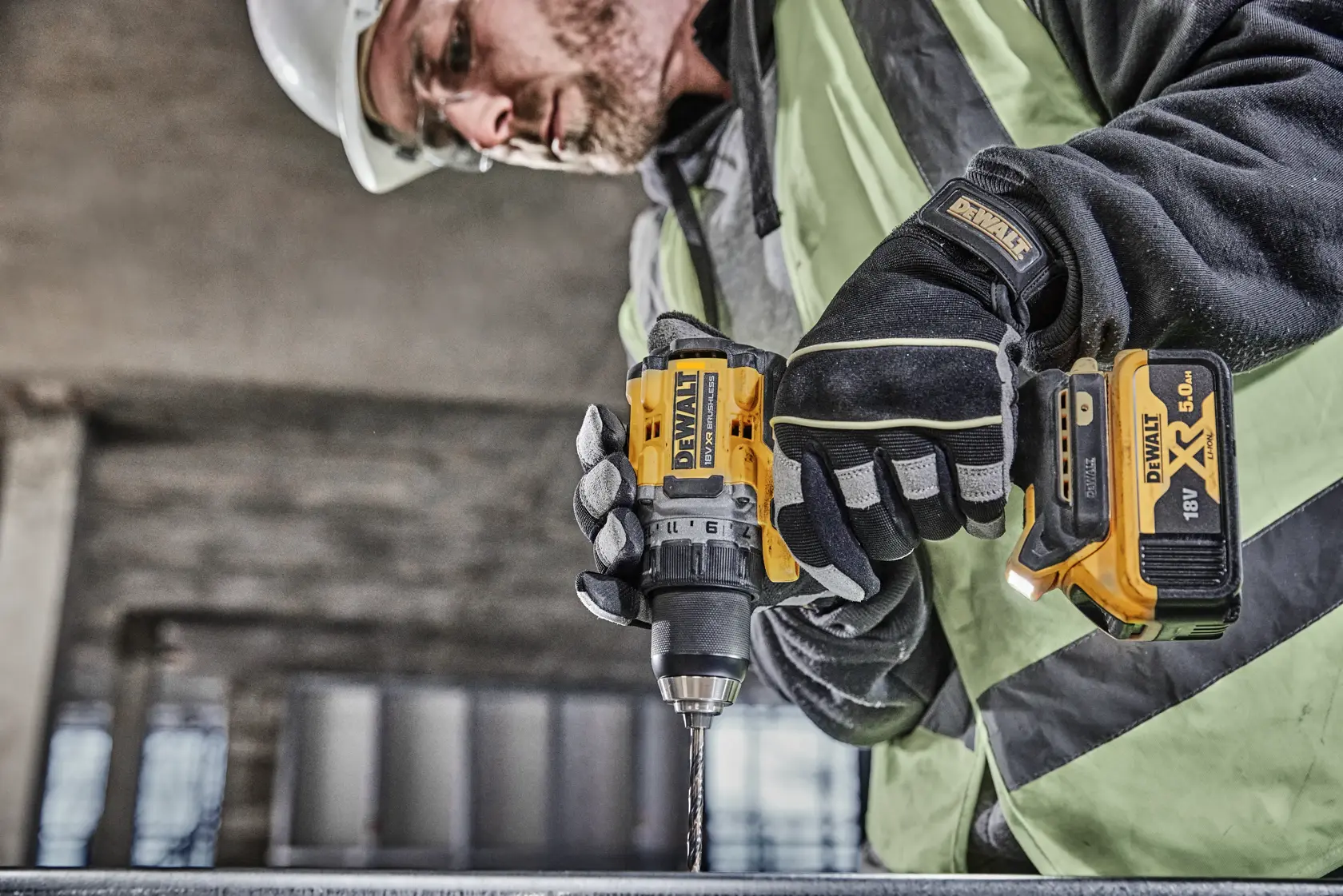 Une personne portant un équipement de sécurité utilise une perceuse sans fil DEWALT DCD800P2T avec une batterie XR 18V, en train de percer une surface métallique sur un chantier.