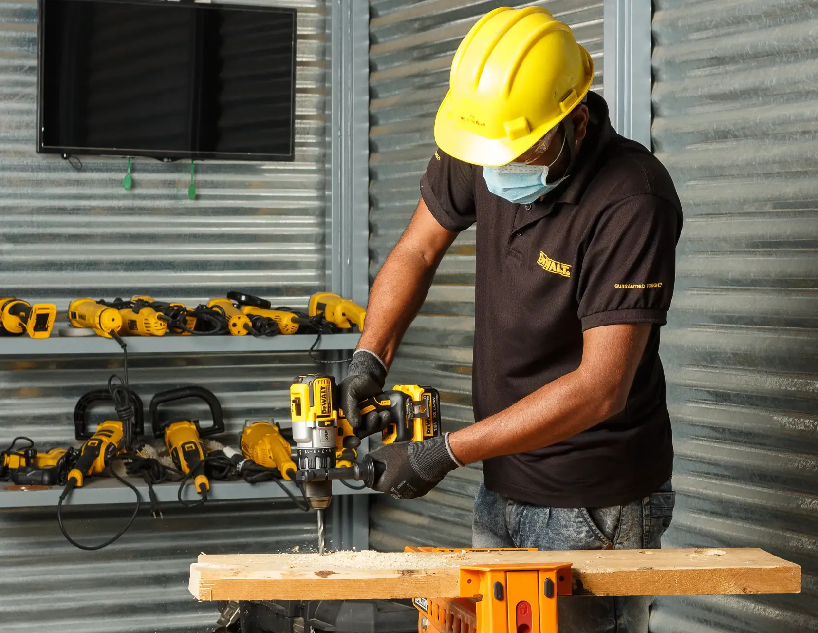Trabajador usa taladro DEWALT DCD996NT en madera, con equipo de protección y herramientas DEWALT detrás.