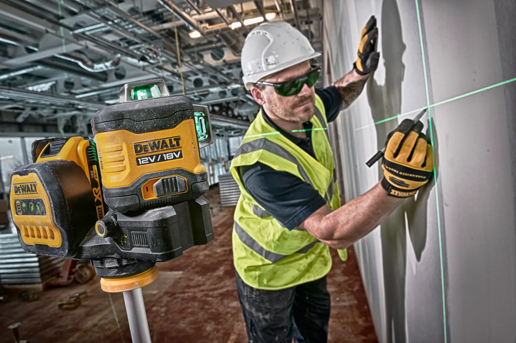 DEWALT Laserlevel zeigt grüne Linien an Wand, Arbeiter markiert und trägt Handschuhe und Helm auf Baustelle.