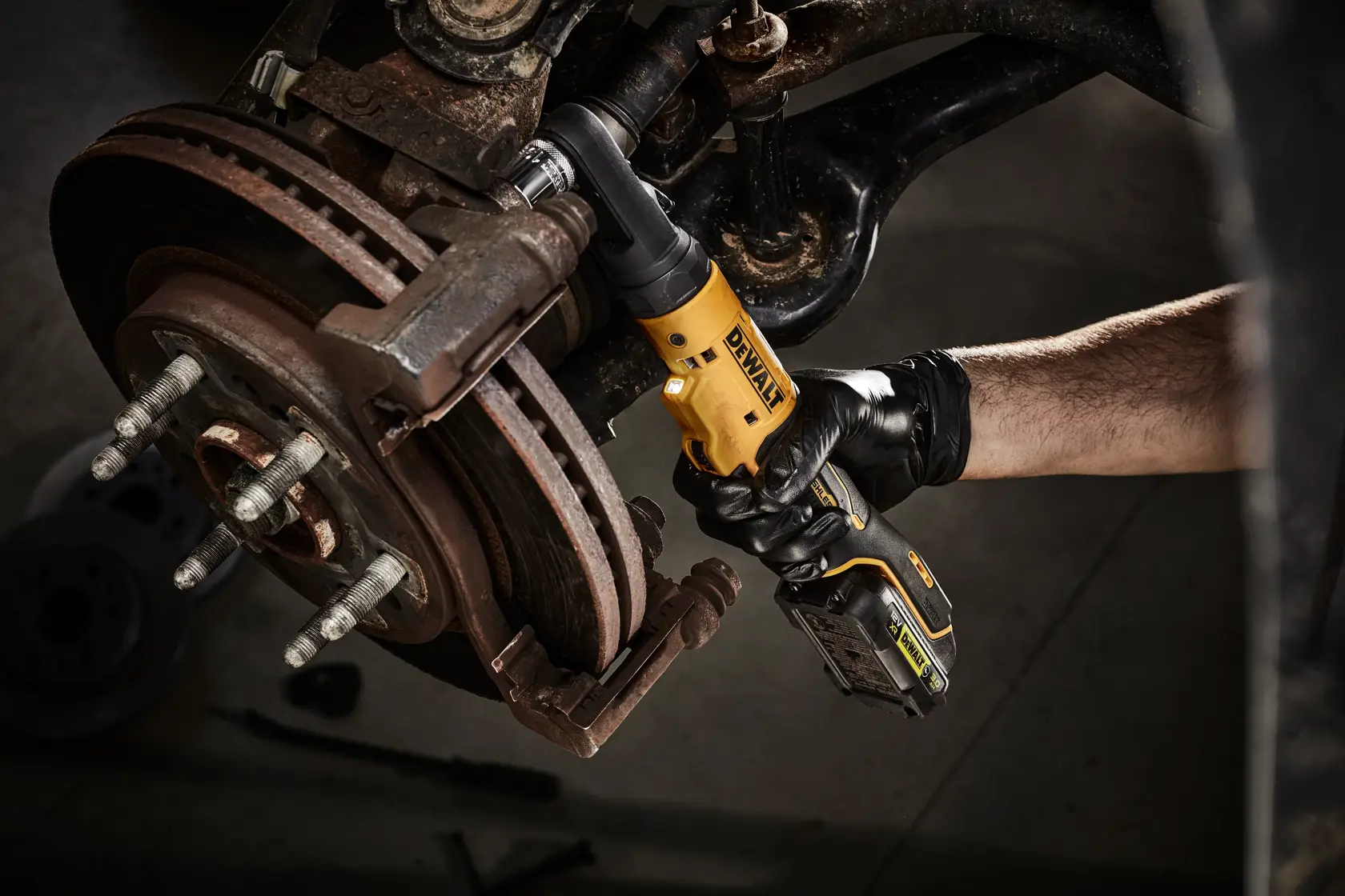 Persona usa herramienta de carraca inalámbrica DEWALT en frenos de coche, con guantes negros.