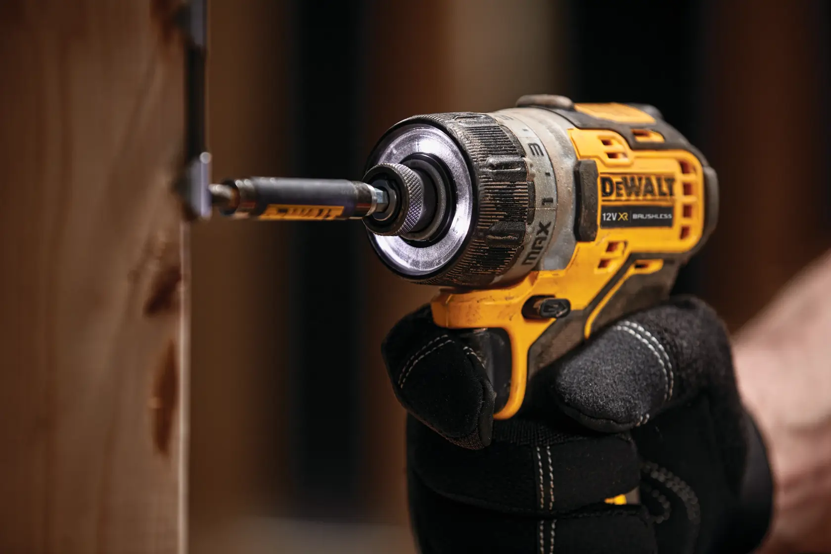 Destornillador inalámbrico DEWALT atornillando en madera, sostenido por una mano con guante.