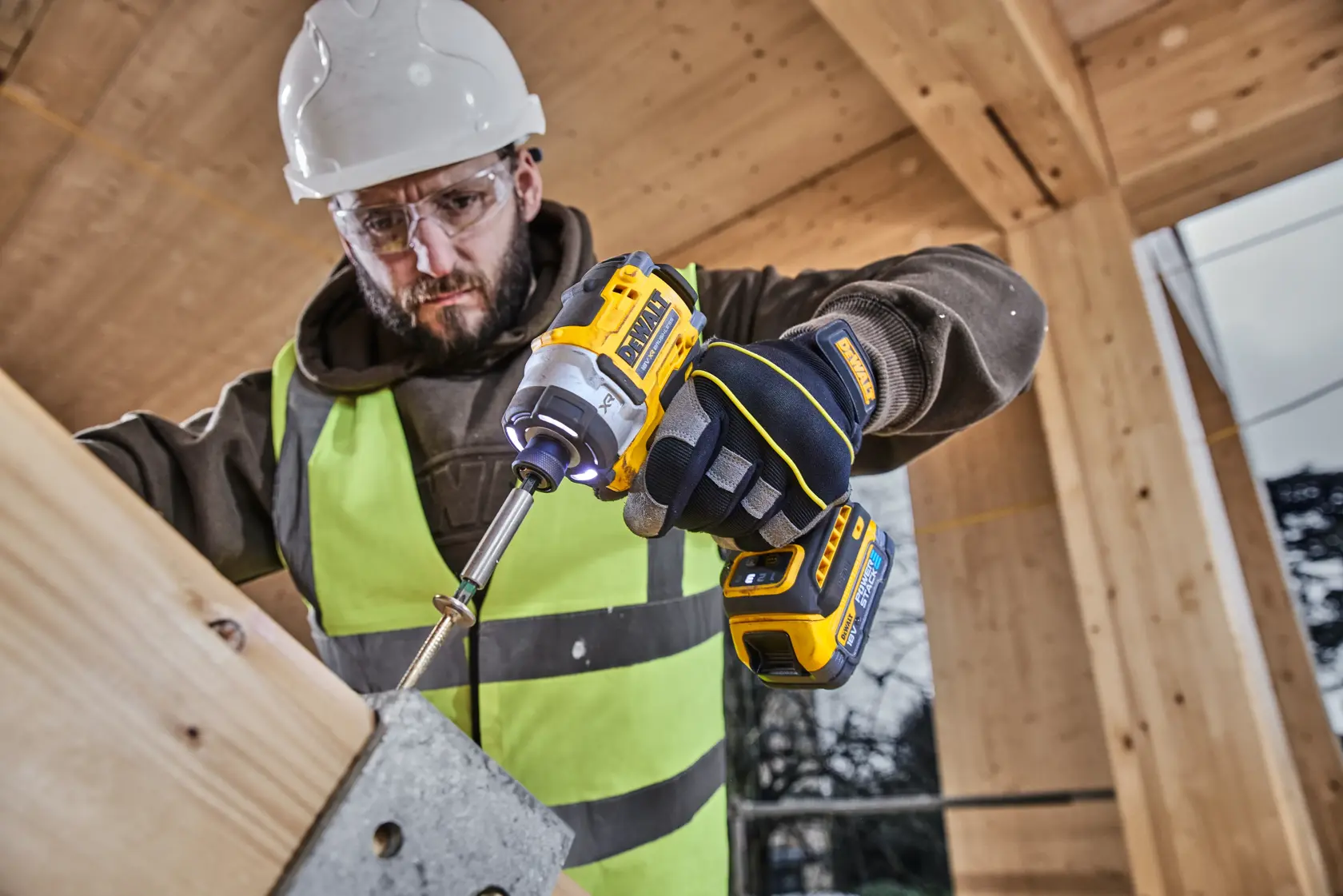Herramientas DEWALT DCK2201P1T1-XE, DCF860NT en obra, trabajador con taladro y guantes.