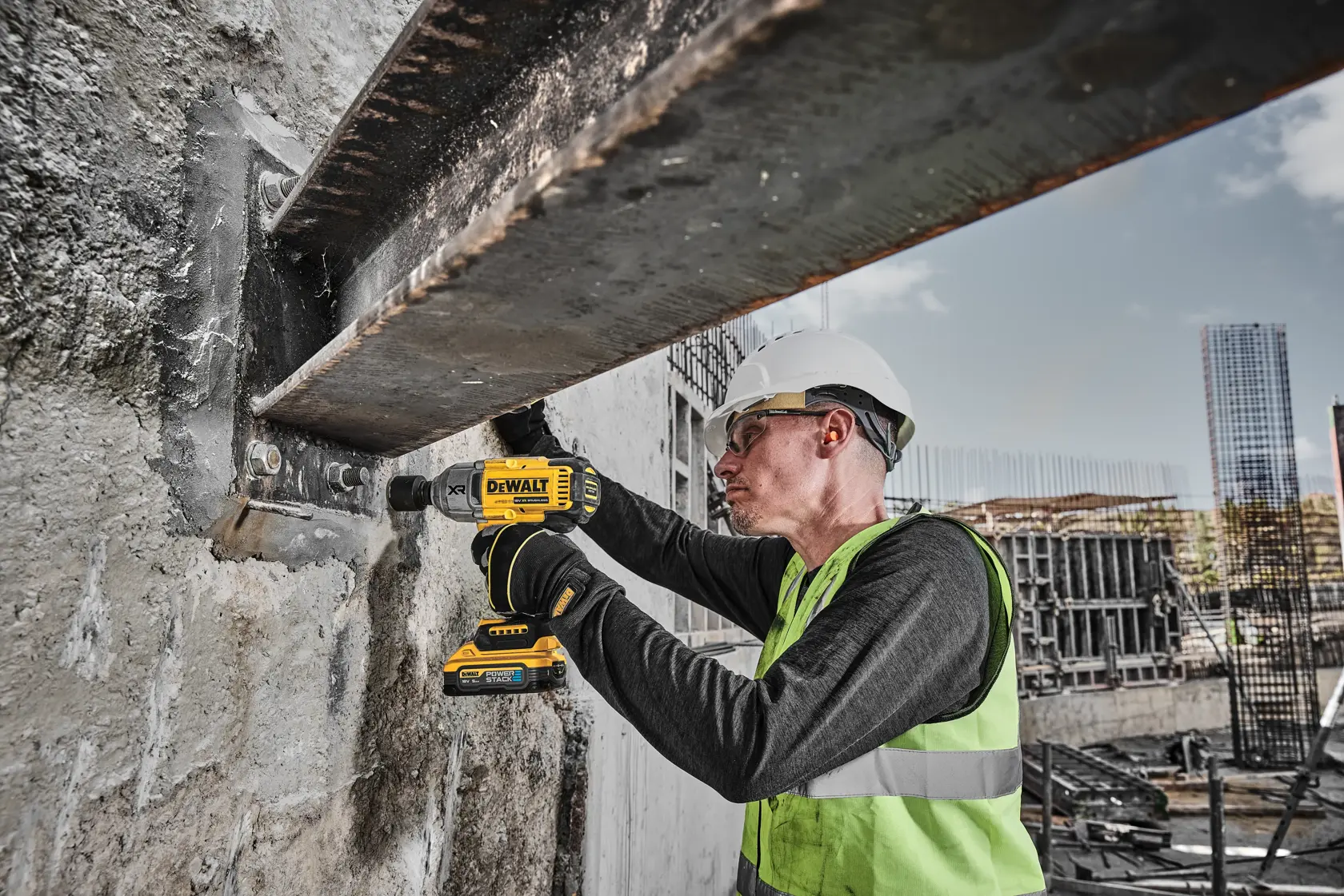 Trabajador usa taladro DEWALT DCF900H2T en una viga de acero, lleva equipo de seguridad y casco.