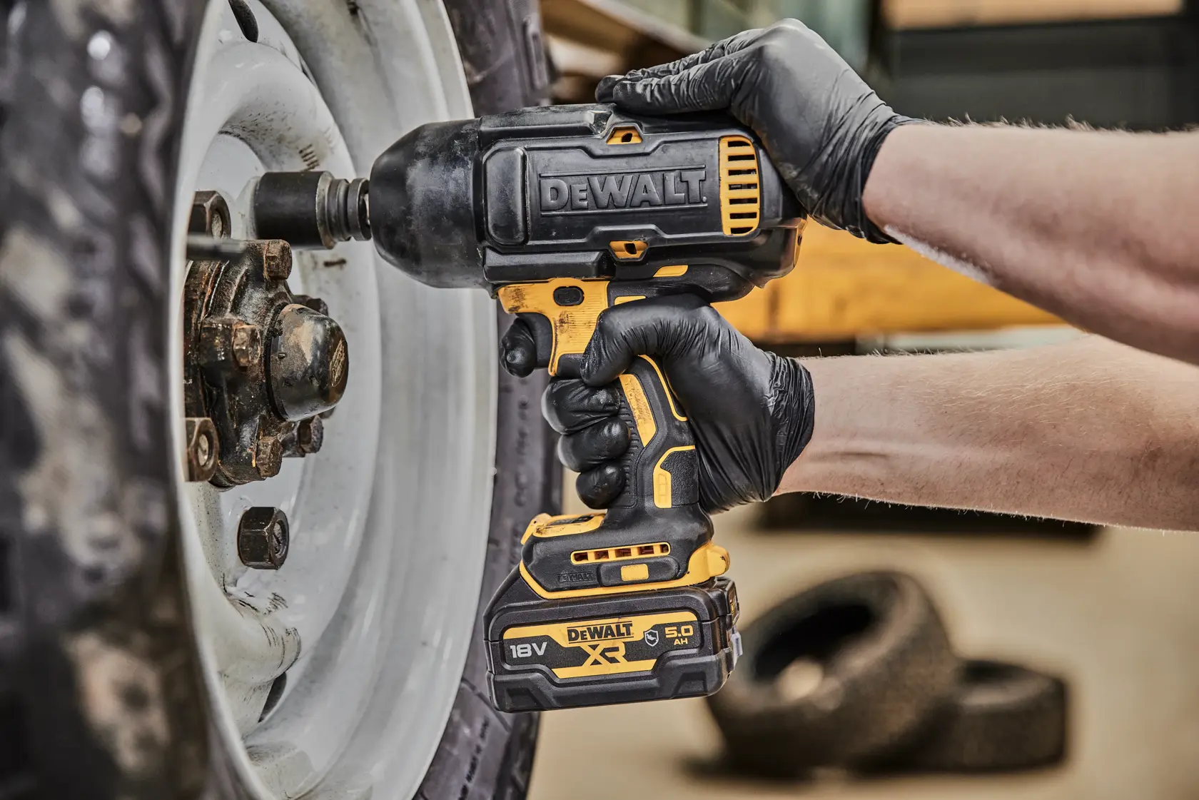 Avvitatore a impulsi DEWALT a batteria rimuove dadi ruota, usato da mano con guanto.