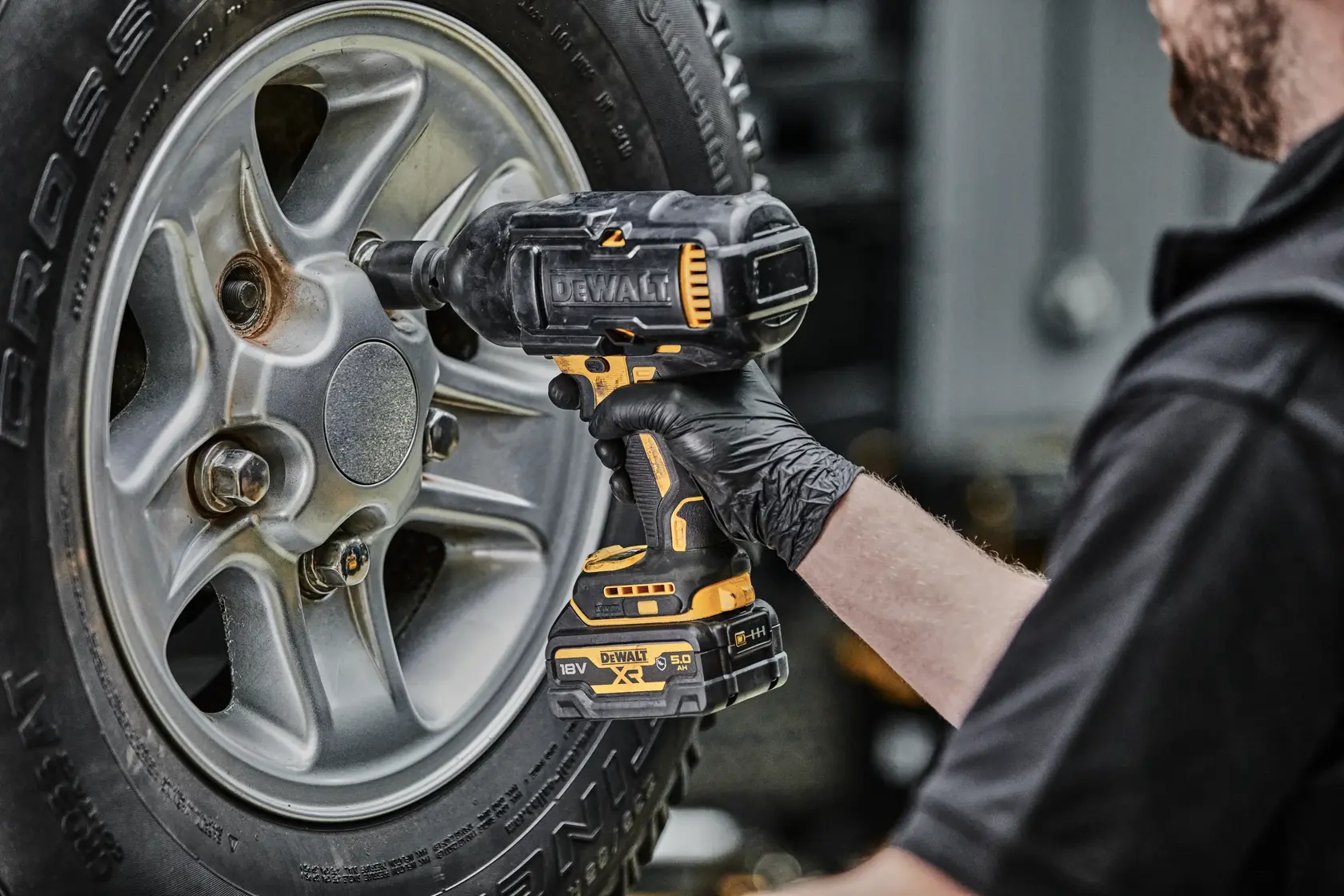 Persona usa un avvitatore a impulsi DEWALT senza fili su un dado ruota di un’auto.