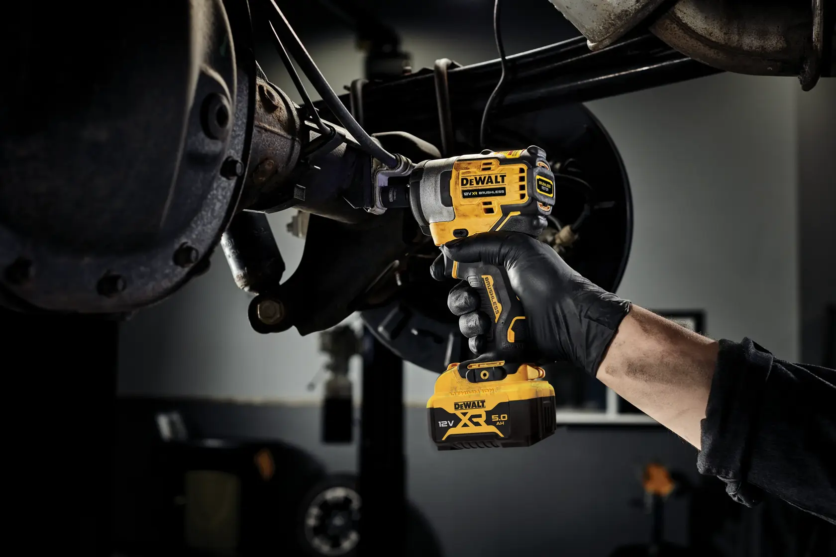Person uses a DEWALT DCF903P1 cordless impact wrench for automotive repair, holding tool near vehicle suspension.