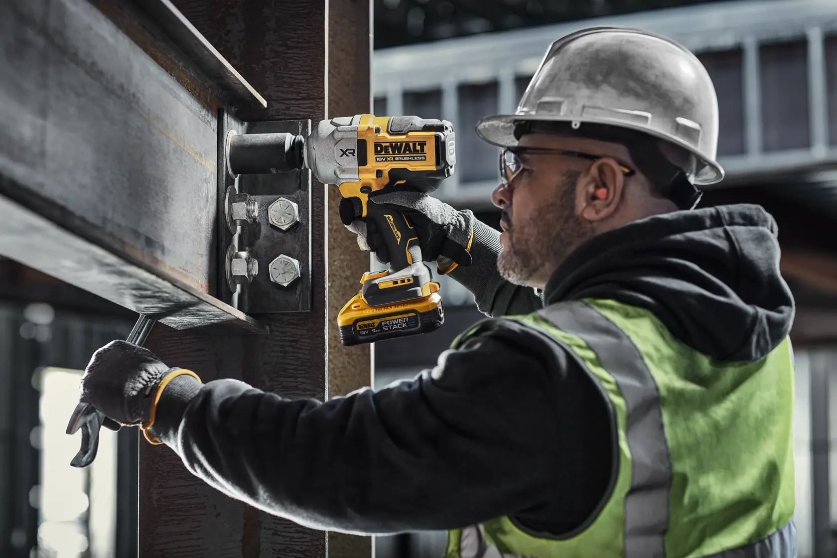 Persona usa avvitatore DEWALT per fissare bulloni su una trave in acciaio in cantiere.