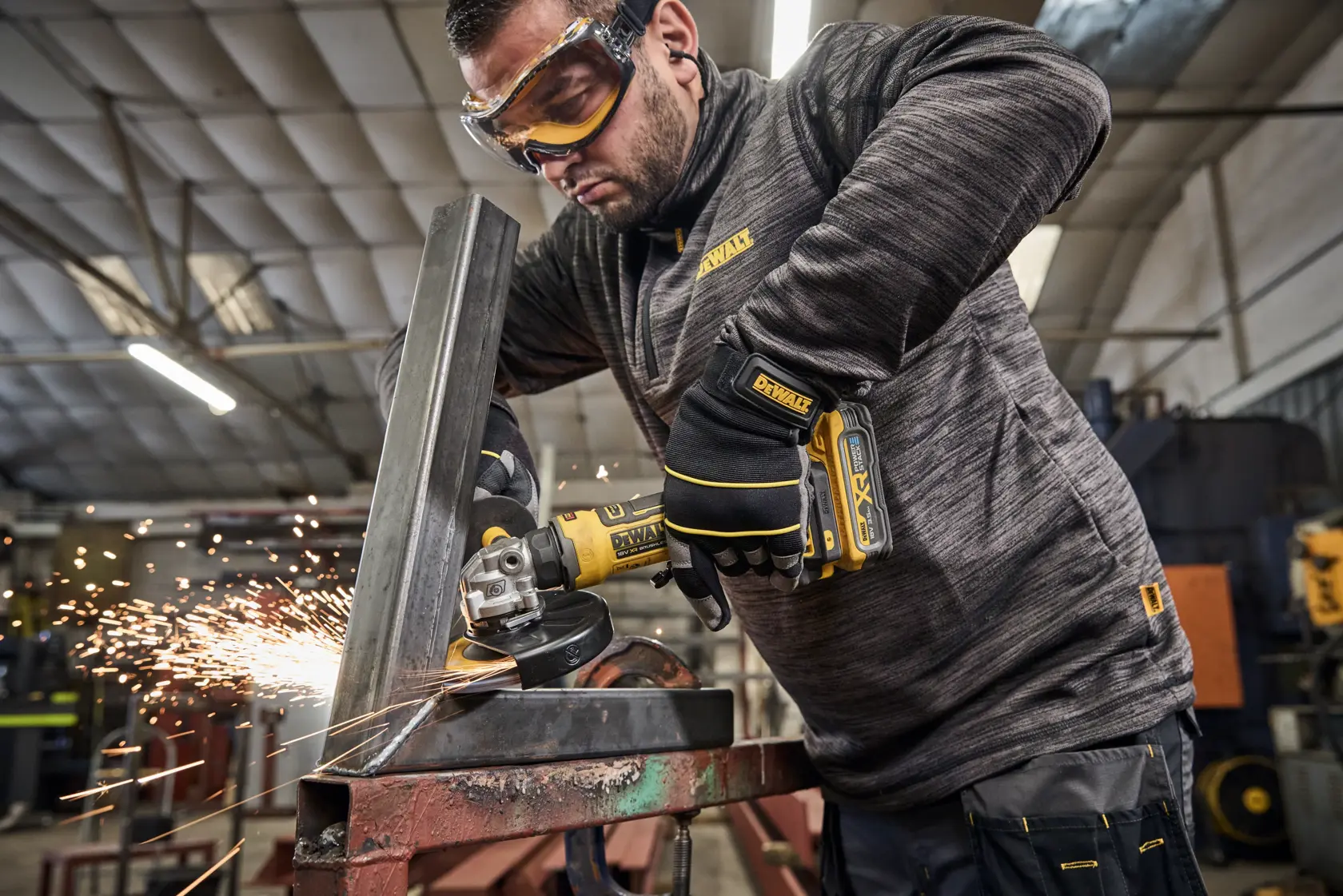 Man uses DEWALT grinder DCG404NT, DCG404S2T-QW on metal, sparks flying, in workshop.