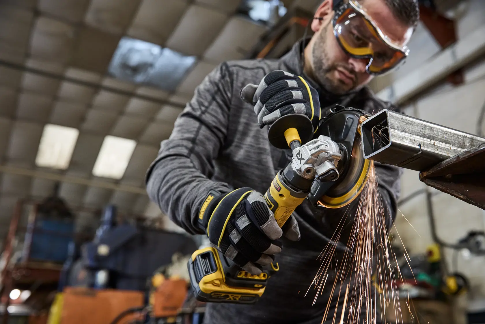 DEWALT DCG404NT, DCG404S2T-QW: worker grinding metal, sparks flying, industrial setting.