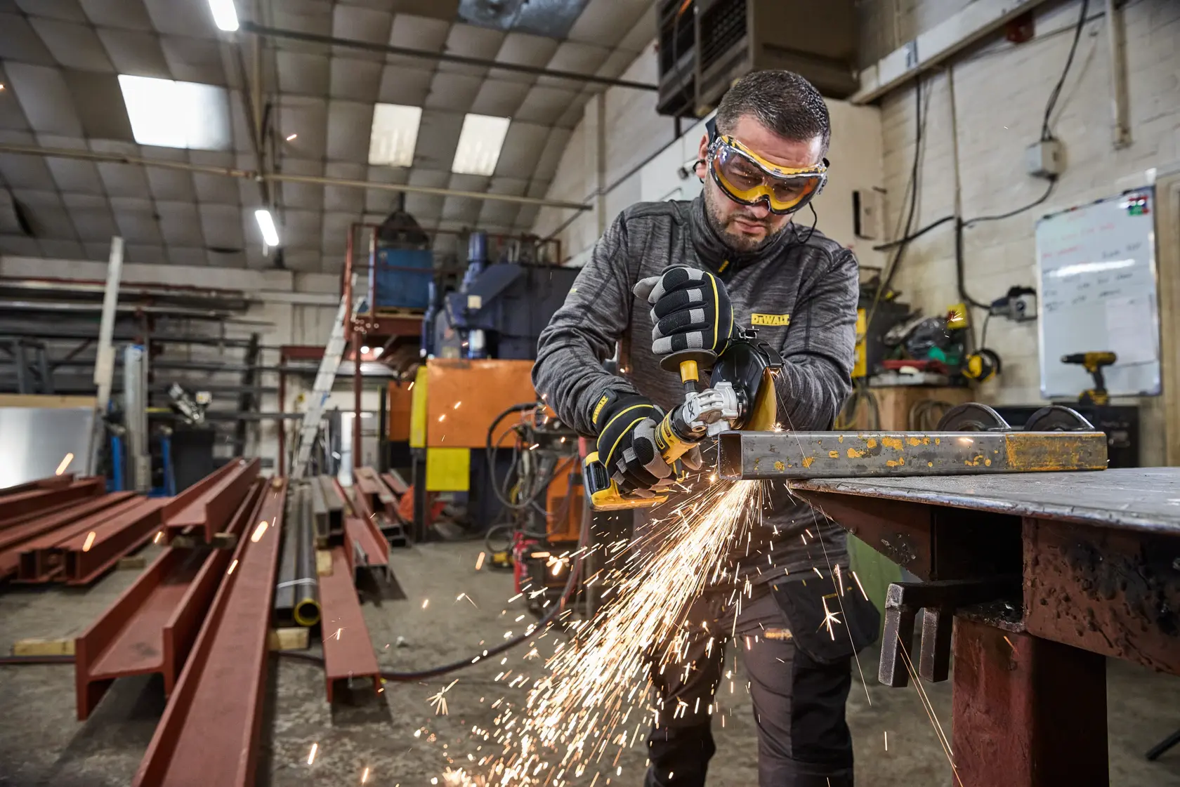 Worker uses DEWALT DCG404S2T-QW, DCG404S2T tool to grind metal in workshop, sparks flying.