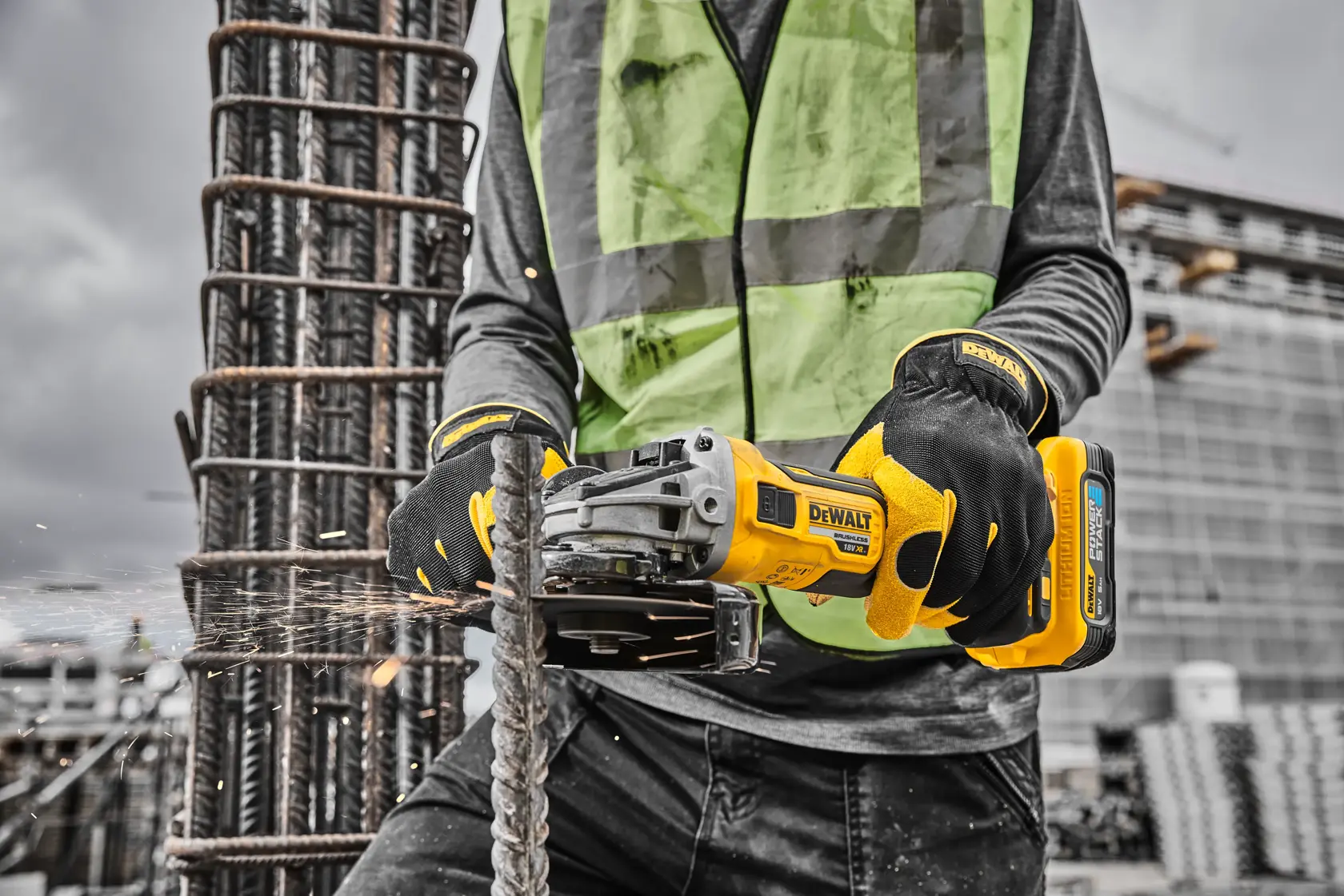 Worker uses a DEWALT cordless grinder to cut rebar on a construction site, wearing gloves and a safety vest.