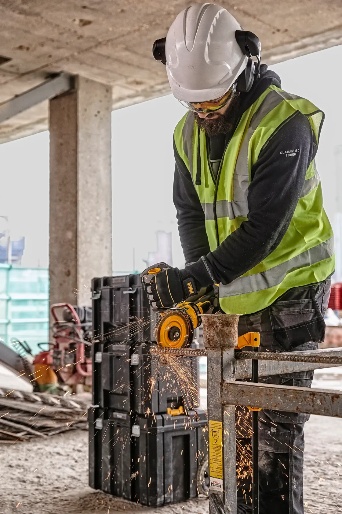 DEWALT DCZ507T2-XE, DCG418N, DCZ503X2-XE tools in use on site. Worker cuts metal; safety gear and sparks visible.