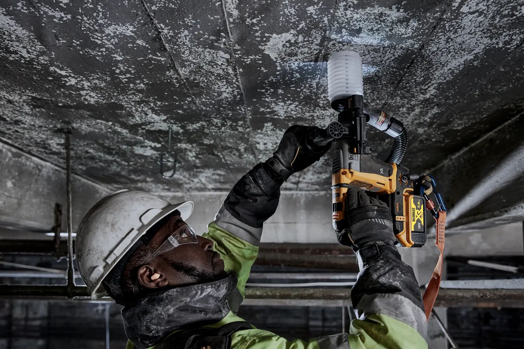 Worker uses DEWALT DCH172P2 rotary hammer drill on a ceiling, wearing safety gear in an industrial setting.