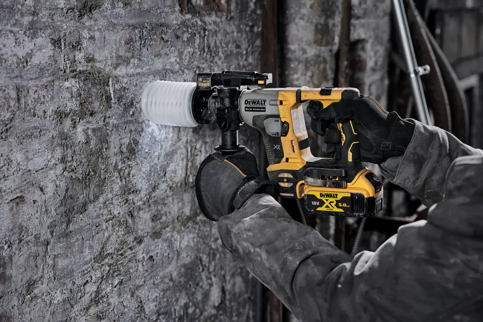 Person using a DEWALT cordless rotary hammer drill to bore into a concrete wall at a construction site.
