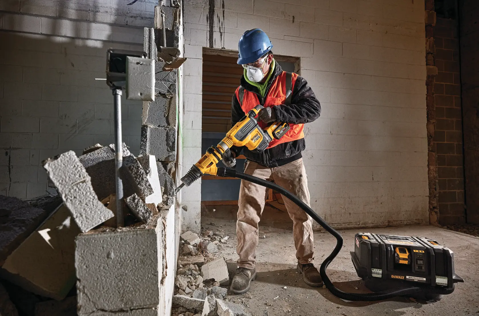 Trabajador usa herramienta DEWALT para romper pared de concreto, con equipo de seguridad y mascarilla.
