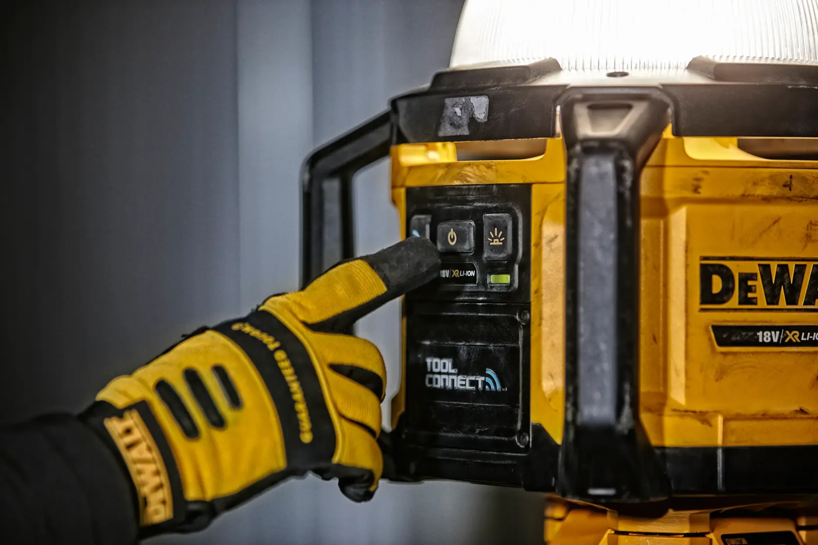 Mano con guante pulsa botón en luz de trabajo DEWALT DCL074 amarilla con Tool Connect.