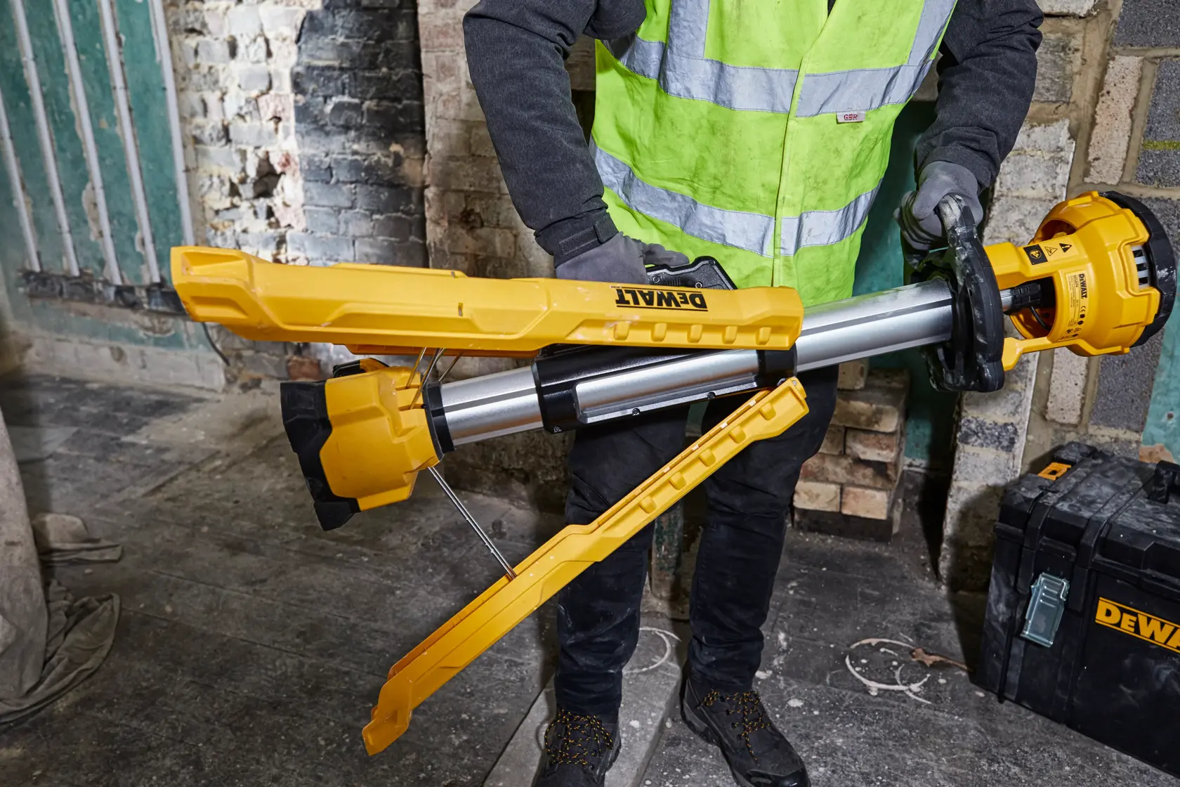 Persona coloca una batería en una lámpara de trabajo DEWALT amarilla con trípode.
