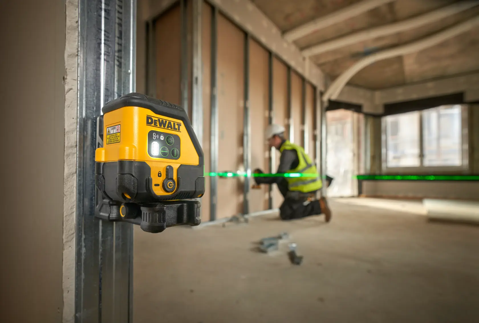 DEWALT-Laser misst grüne Linie auf Baustelle. Arbeiter installiert Wandpaneele mit Warnweste.