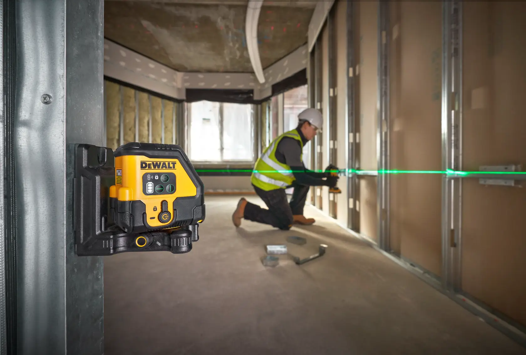 DEWALT-Laser auf Wand, projiziert grüne Linie. Arbeiter richtet Bau­materialien im unfertigen Raum aus.