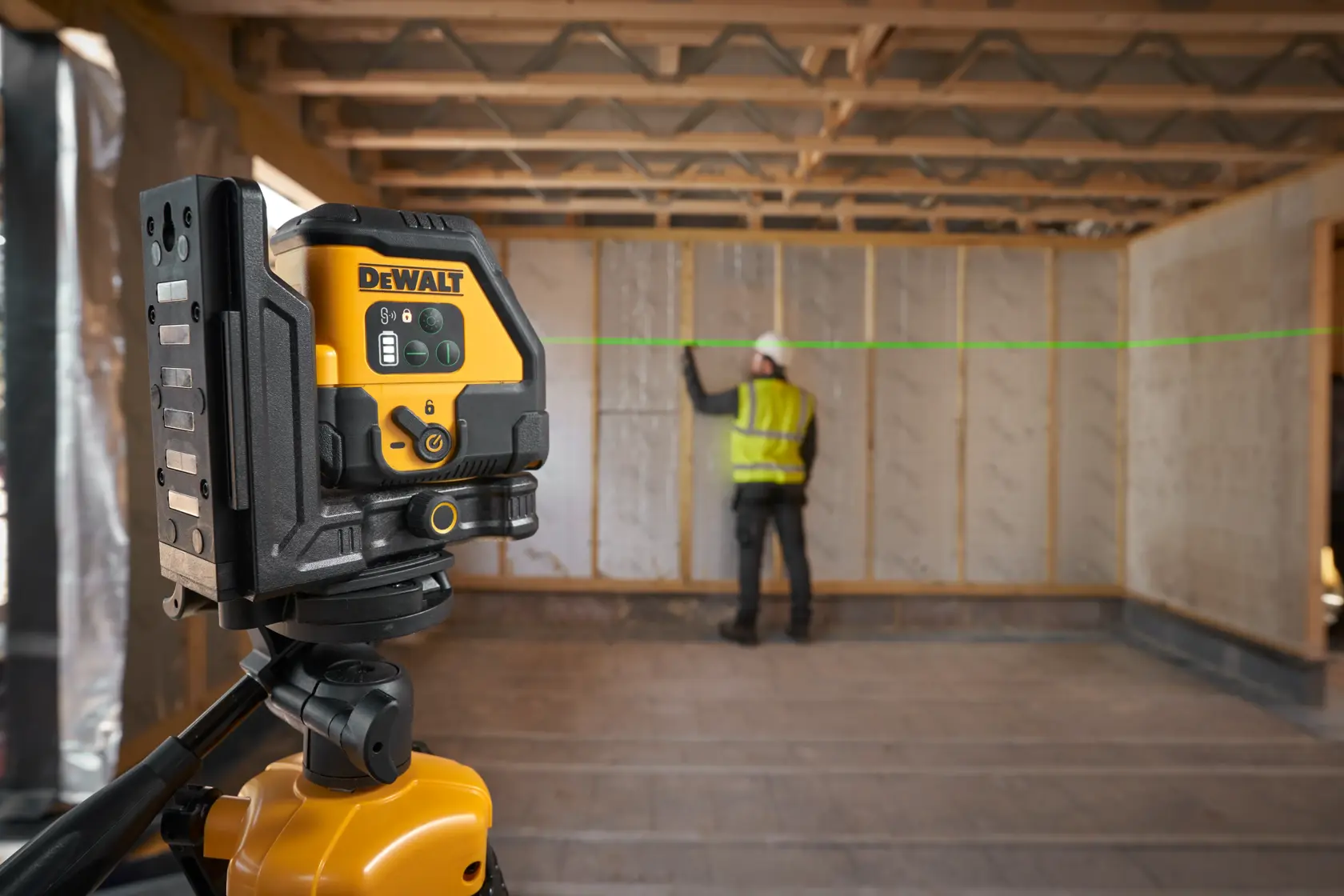 DEWALT-Laser auf Stativ projiziert grünen Strahl in Baustellenraum, Arbeiter markiert Wand.
