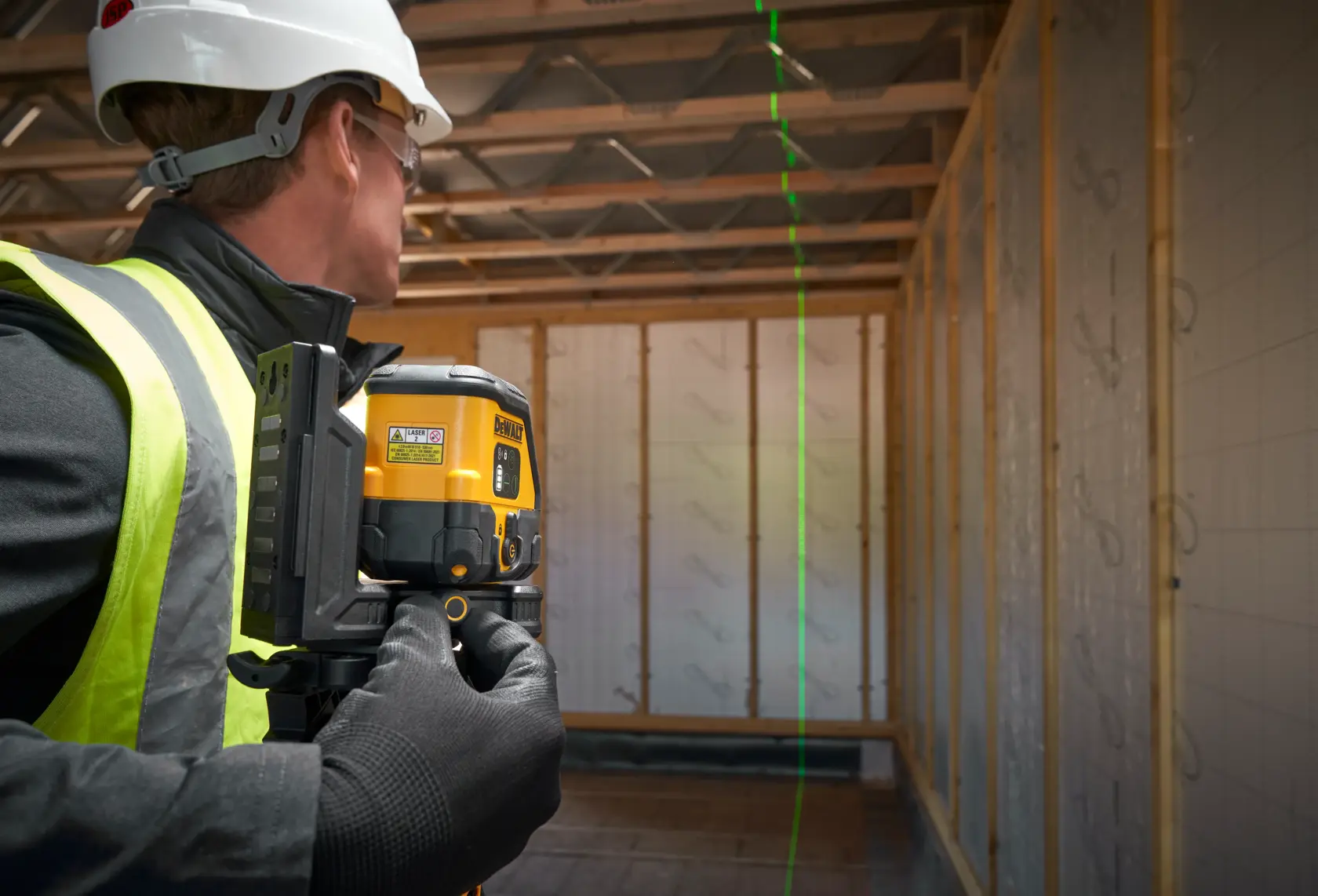 Arbeiter nutzt DEWALT Laser-Nivelliergerät im Rohbau, projiziert eine vertikale grüne Linie.