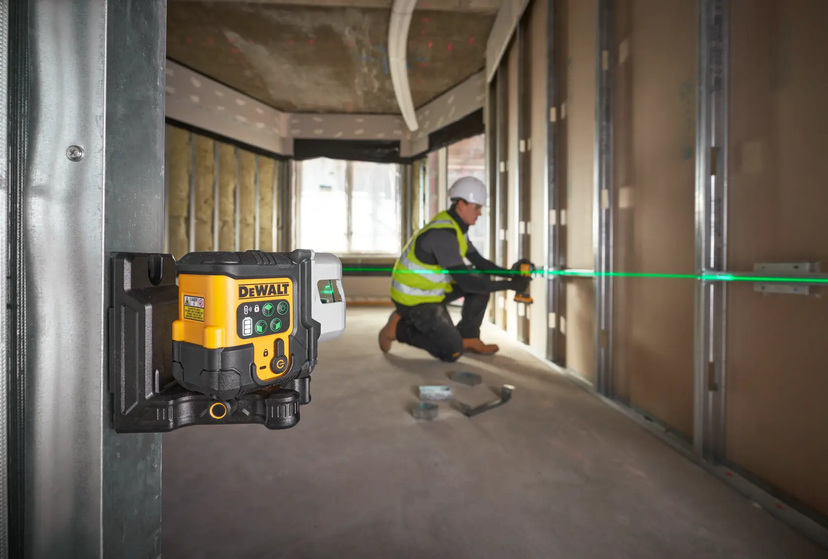 DEWALT-Laser auf Stativ projiziert grüne Linie, Arbeiter markiert Wand auf Baustelle.