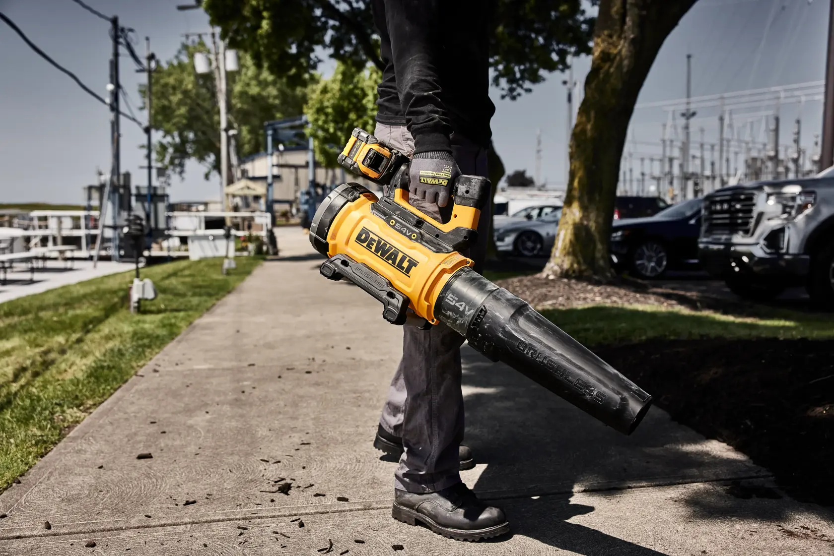 Persona usando soplador de hojas DEWALT amarillo inalámbrico en una acera al aire libre.