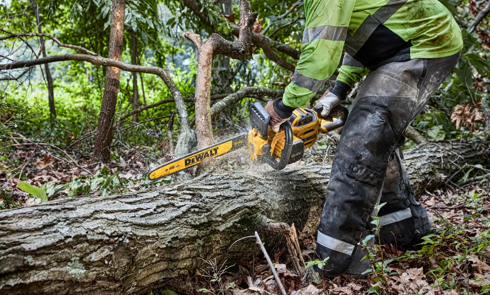 Eine Person benutzt eine kabellose Kettensäge von DEWALT, um einen umgestürzten Baumstamm im Freien in einem bewaldeten Gebiet zu schneiden.