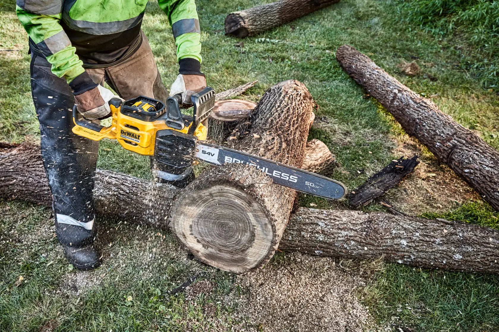 Eine Person benutzt eine kabellose DEWALT Kettensäge, um draußen einen großen Holzstamm zu schneiden, wobei Holzspäne und