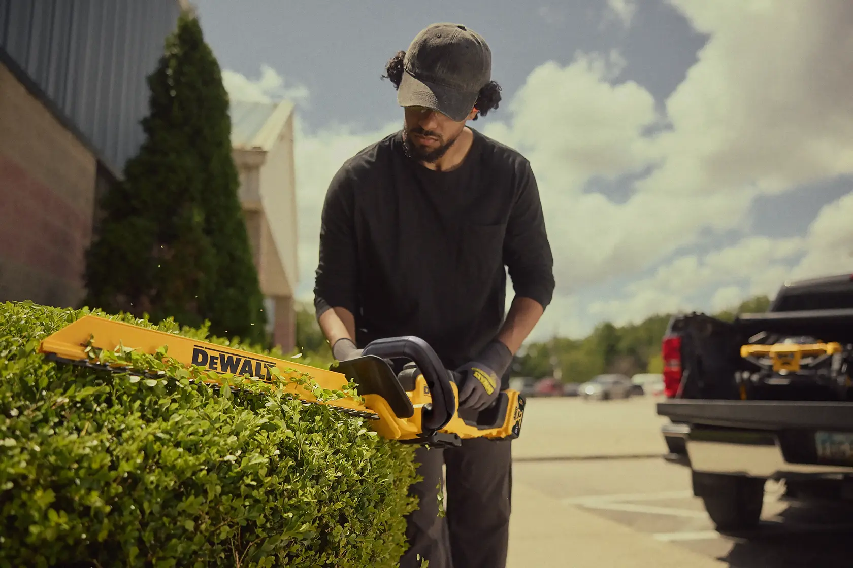 Person schneidet eine Hecke mit einem DEWALT Akku-Heckenschneider draußen bei einem geparkten Lkw.