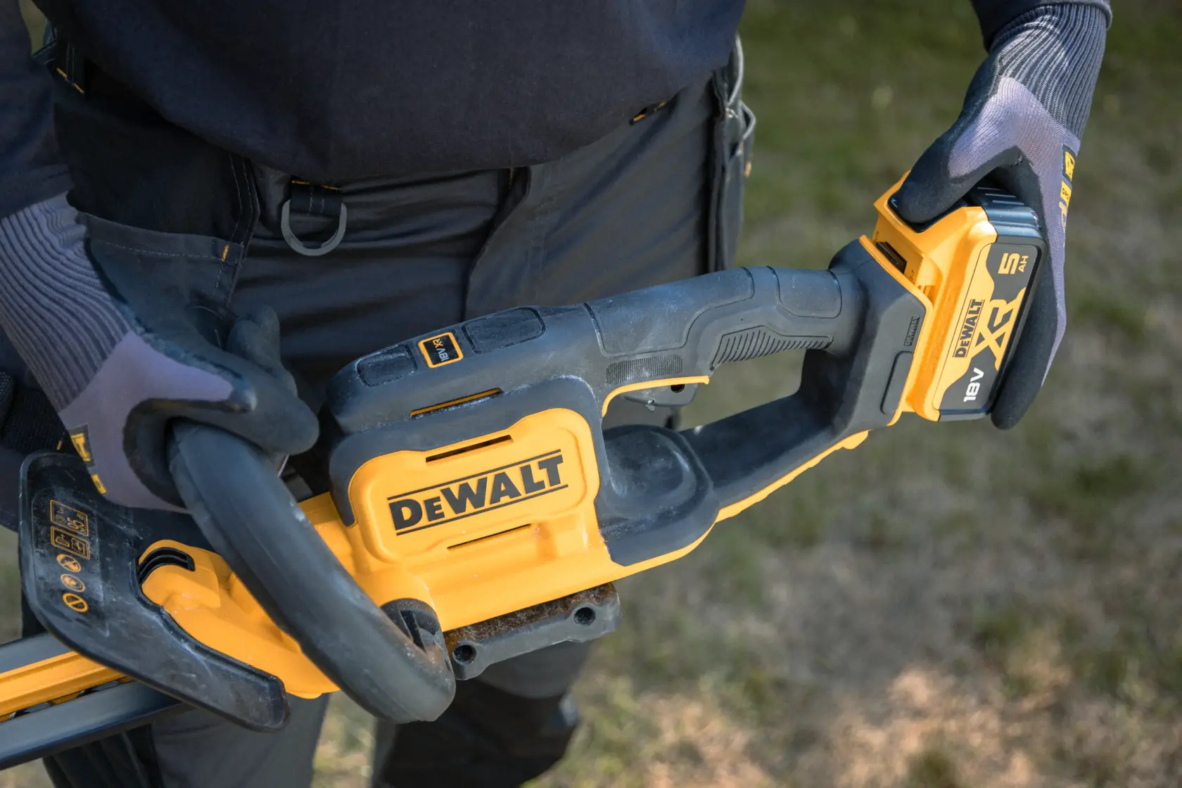 Primo piano di guanti che tengono un tagliasiepi DEWALT a batteria all'aperto.