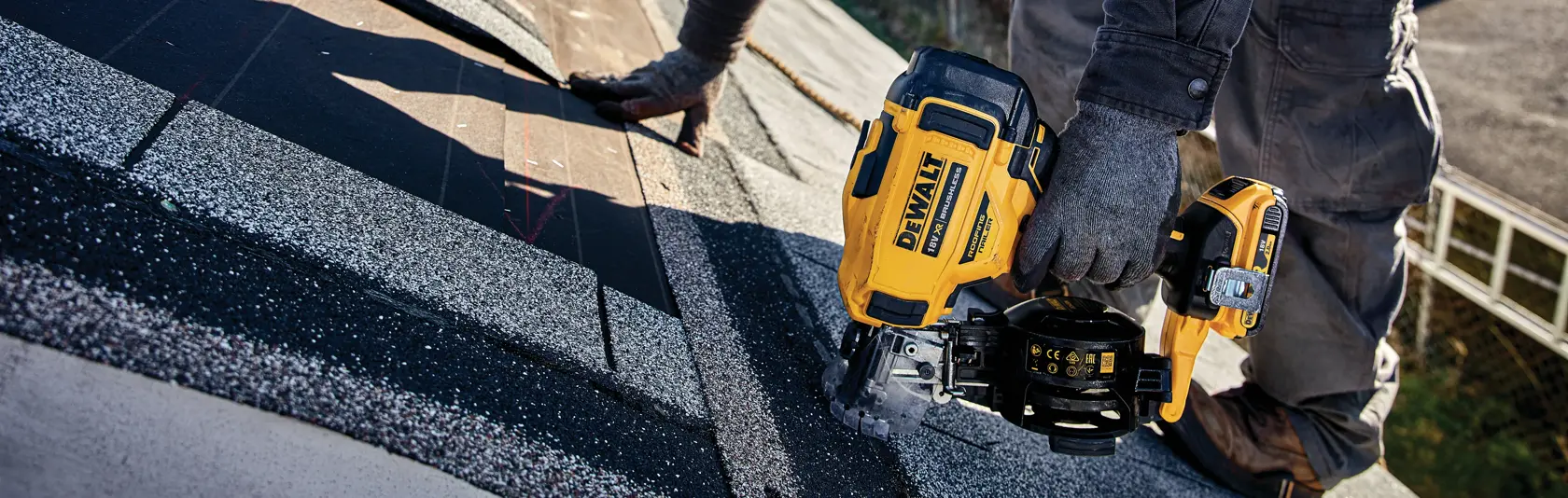 Worker uses DEWALT cordless nailer on roof shingles during installation.