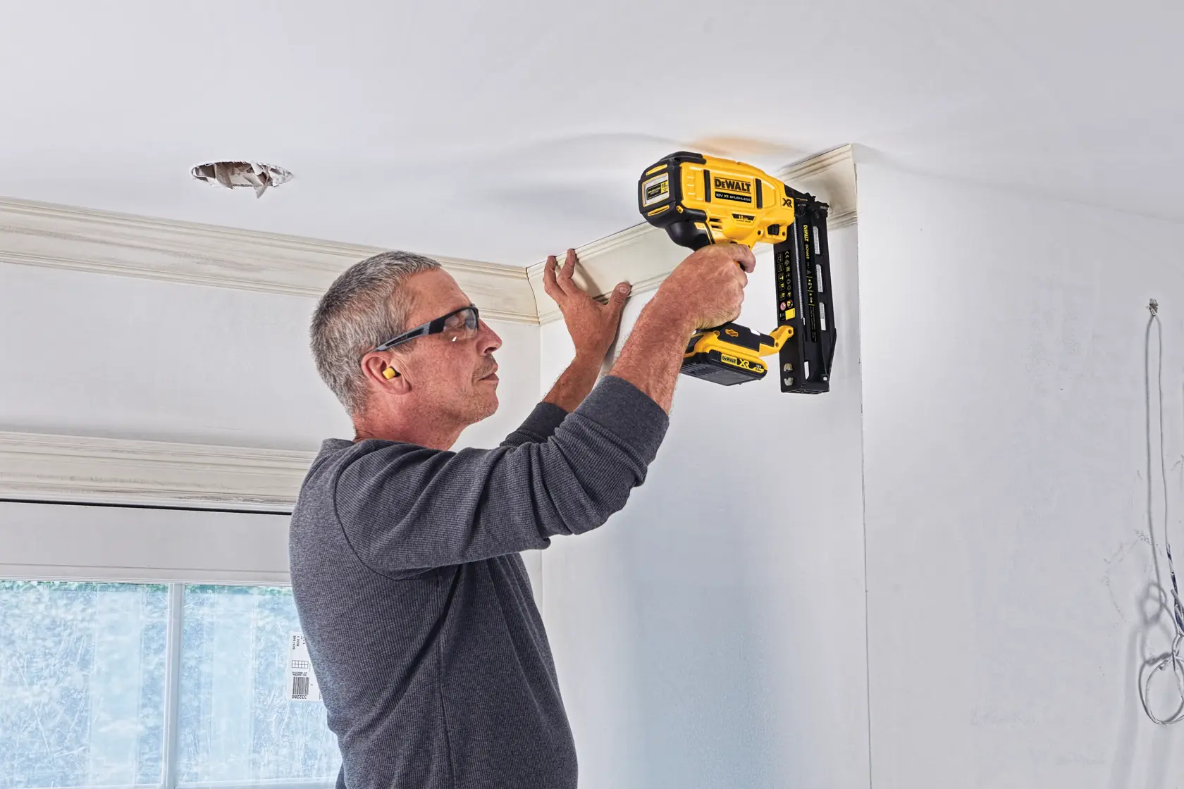 Persona usa clavadora DEWALT DCN662N para fijar moldura al techo en una habitación iluminada.