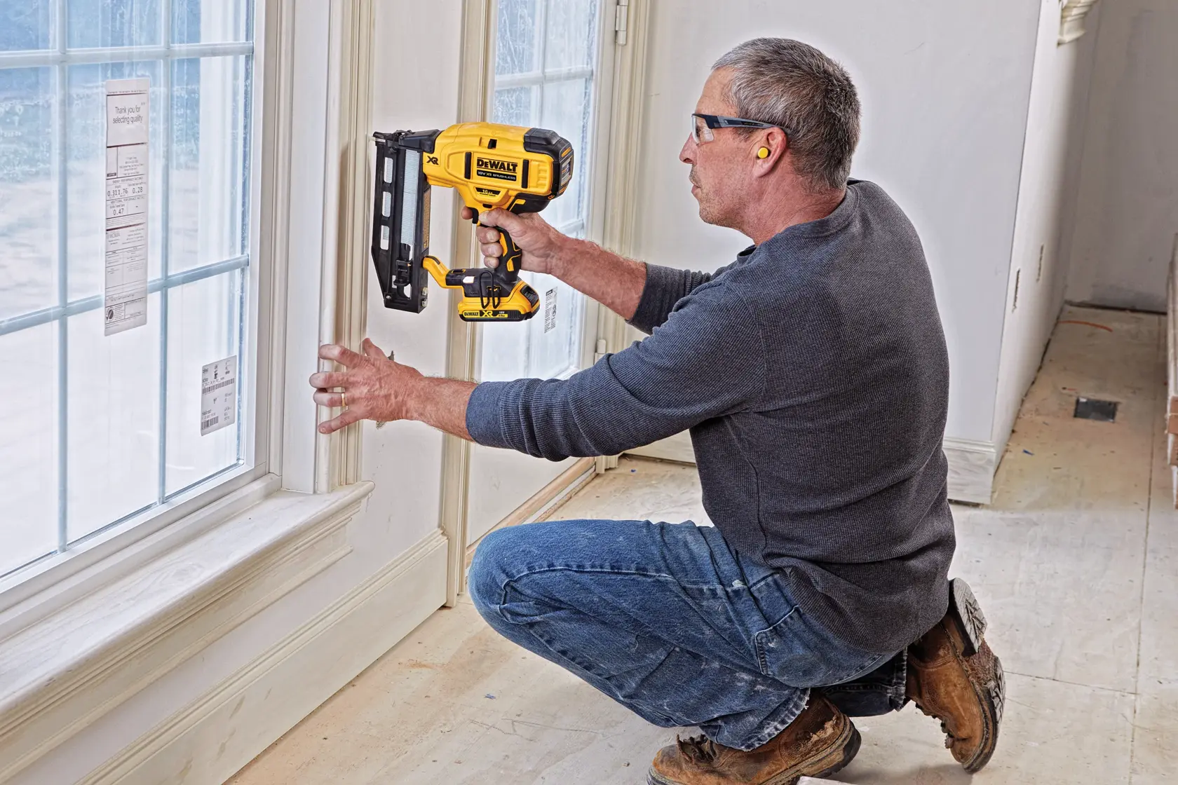 Persona utiliza una clavadora DEWALT para fijar moldura cerca de una ventana en interiores.