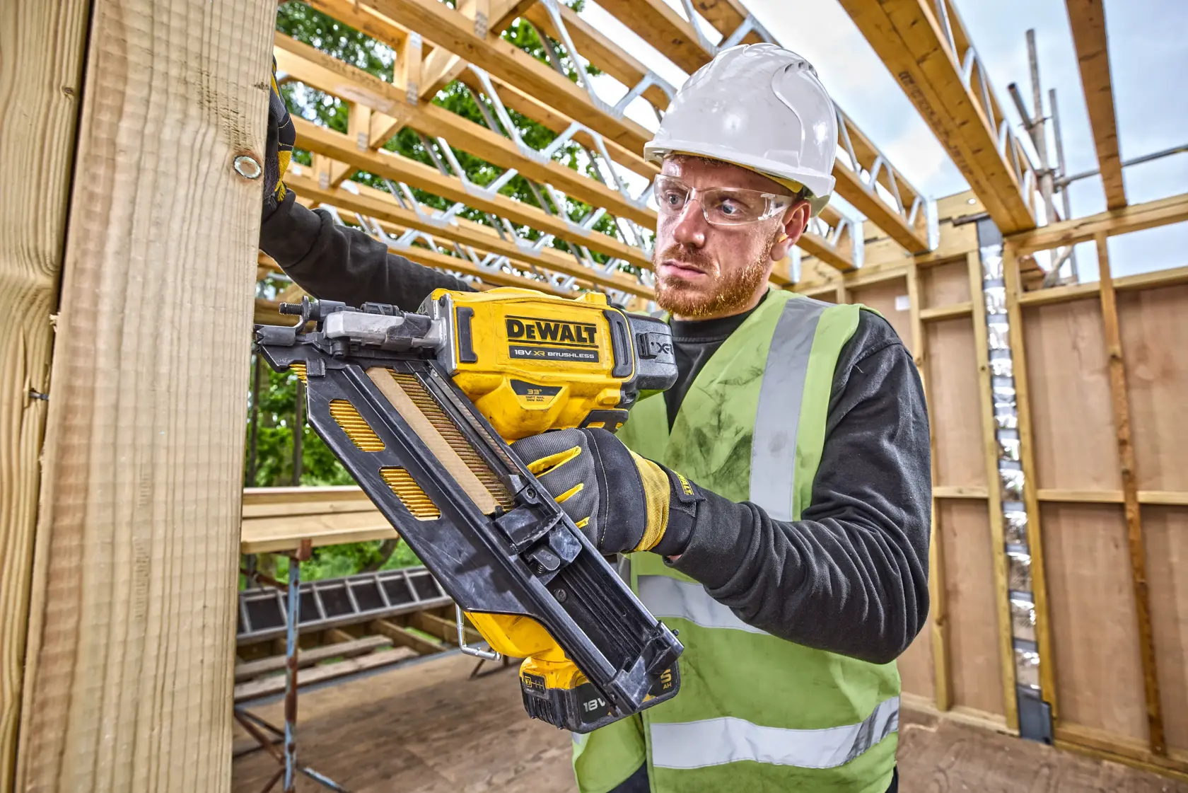 Persona usando clavadora DEWALT DCN930N en construcción, con equipo de seguridad y vigas de madera.