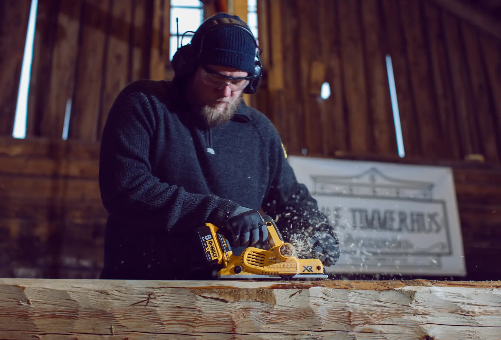 Personne utilisant une raboteuse DEWALT DCP580P2 sur une poutre en bois dans un atelier.