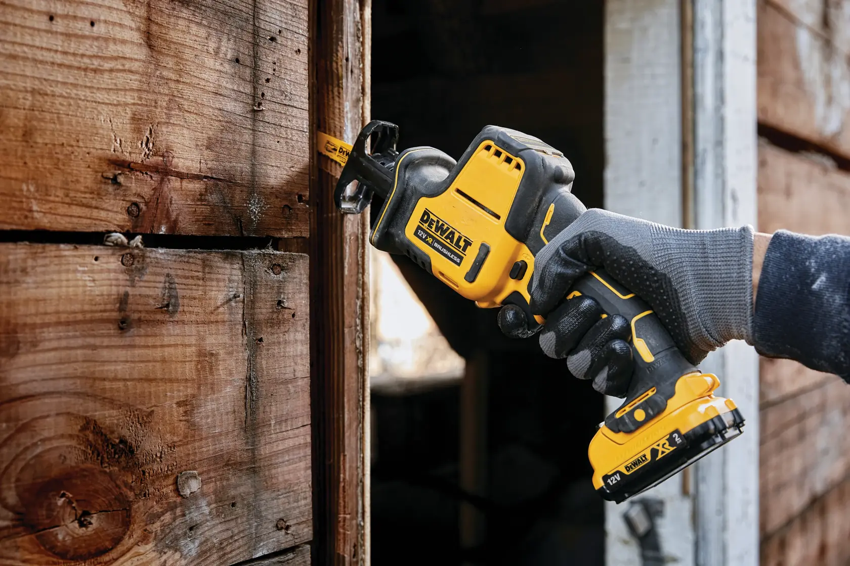 Sierra recíproca DEWALT inalámbrica cortando madera, sostenida por mano enguantada en carpintería exterior.