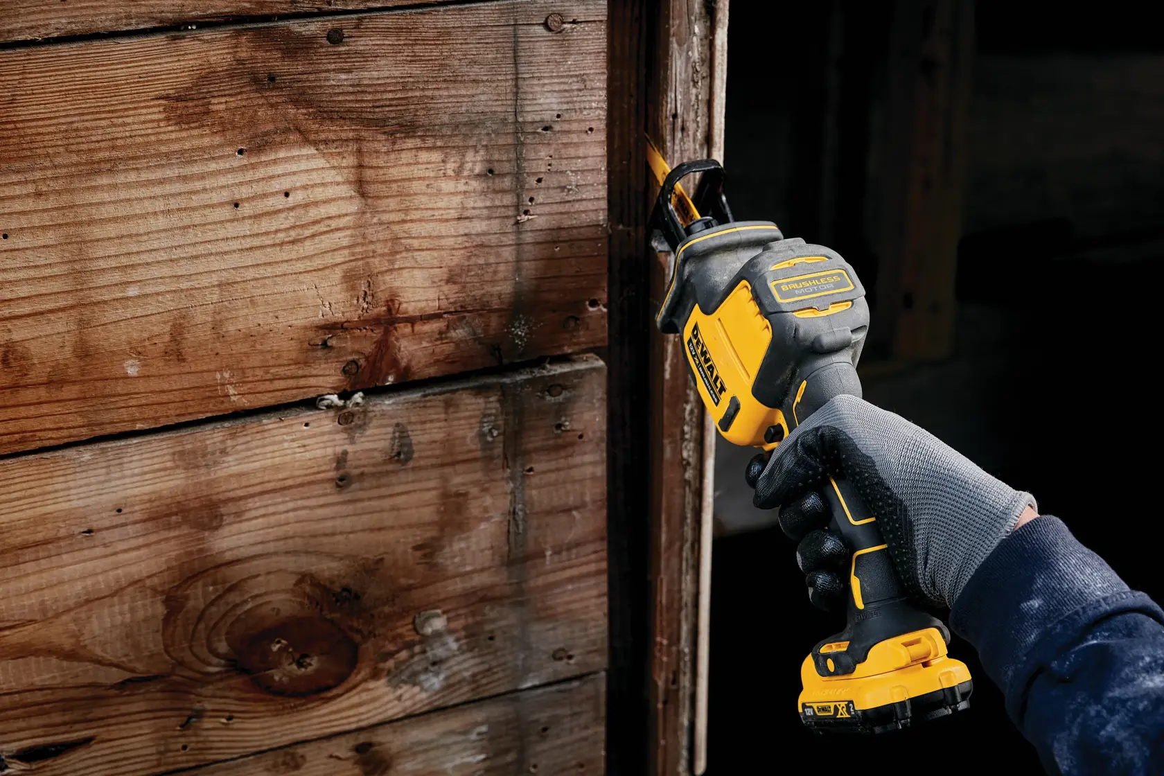 Persona usa una sierra recíproca DEWALT para cortar madera junto a una pared, sujetando la herramienta con guante.