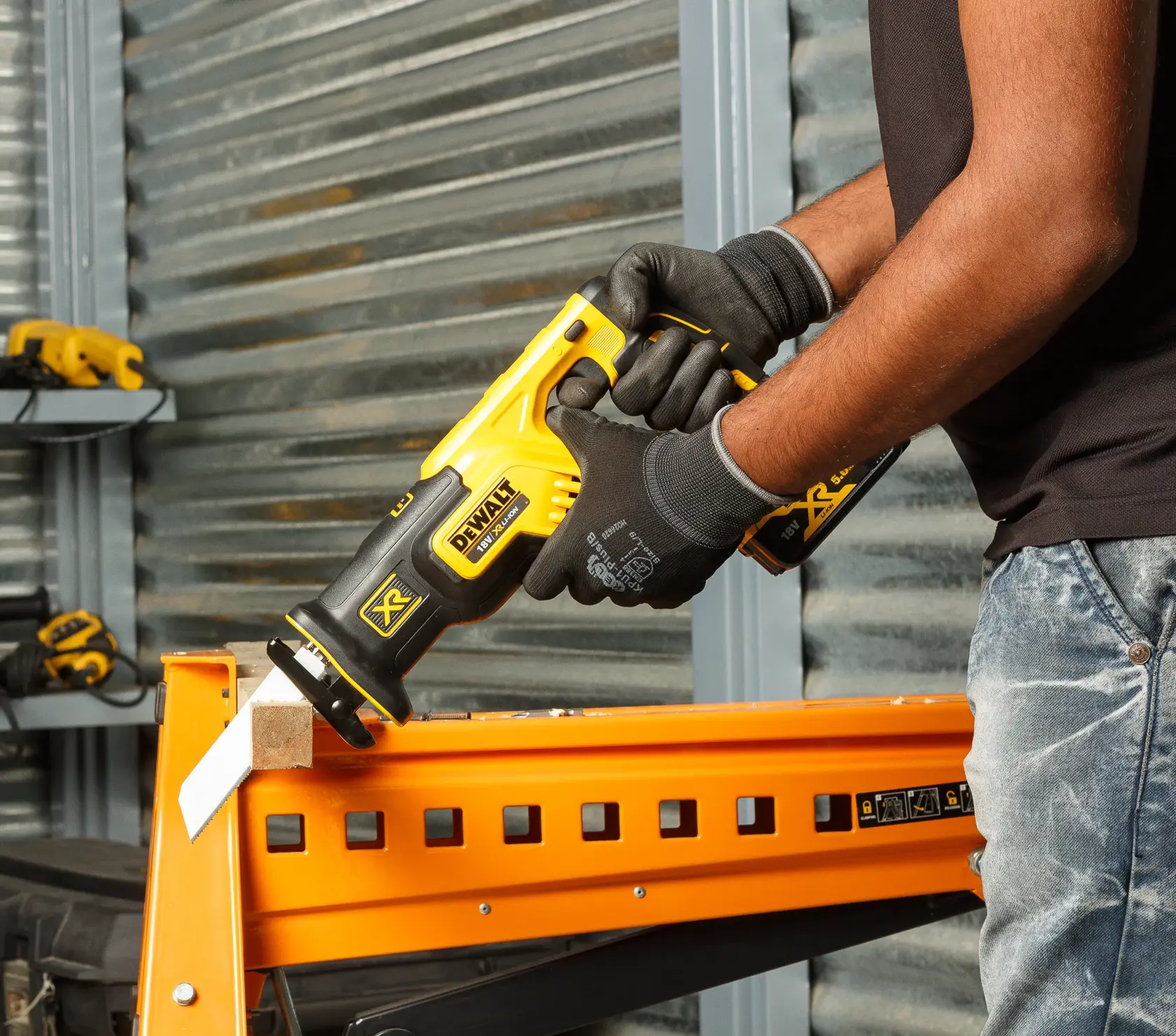 Une personne utilise une scie sabre DEWALT DCS367P2 pour couper du bois sur un établi orange en atelier.