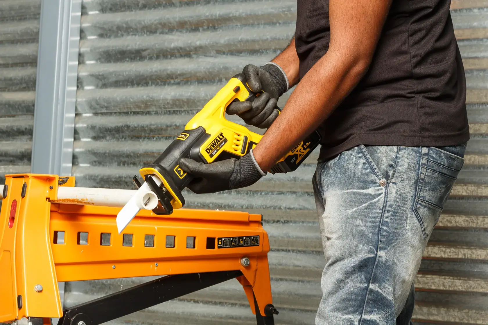 Personne utilise la scie DEWALT DCS367P2 pour couper un tuyau sur un établi jaune.