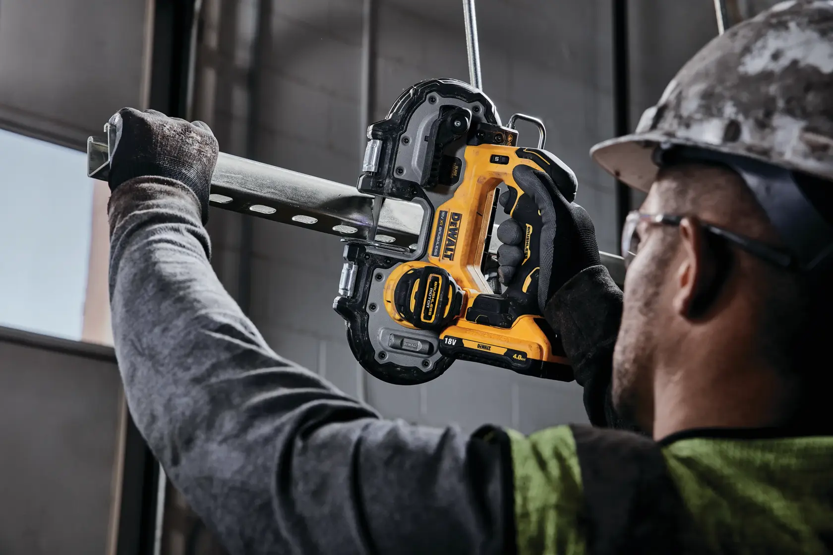 Personne utilisant une scie à ruban DEWALT sans fil pour couper un tuyau en métal, avec gants et casque.