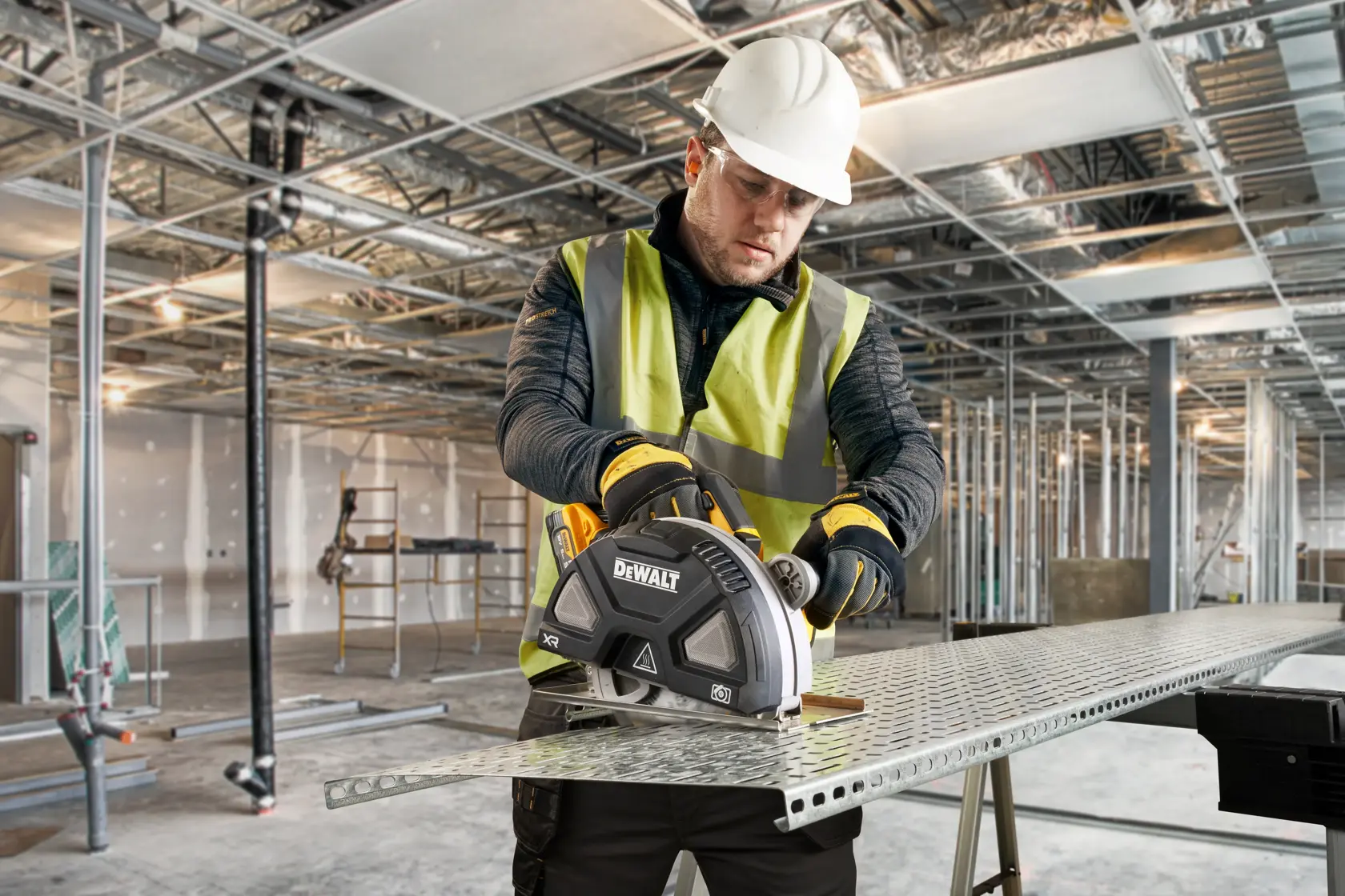 Worker uses DEWALT metal cutting saw on a steel sheet in a construction setting with safety gear.
