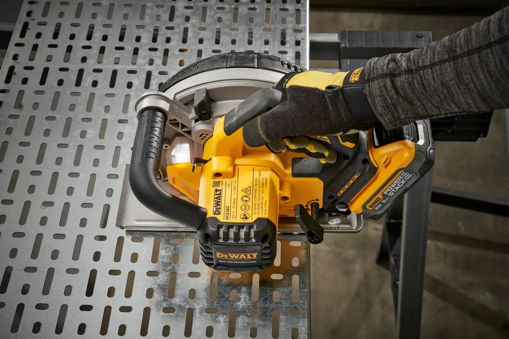 Gloved hand uses a yellow DEWALT cordless saw to cut a metal sheet on a worktable.