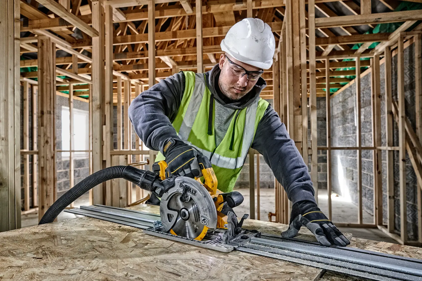 Trabajador usa sierra circular DEWALT con guía sobre madera en edificio en construcción.