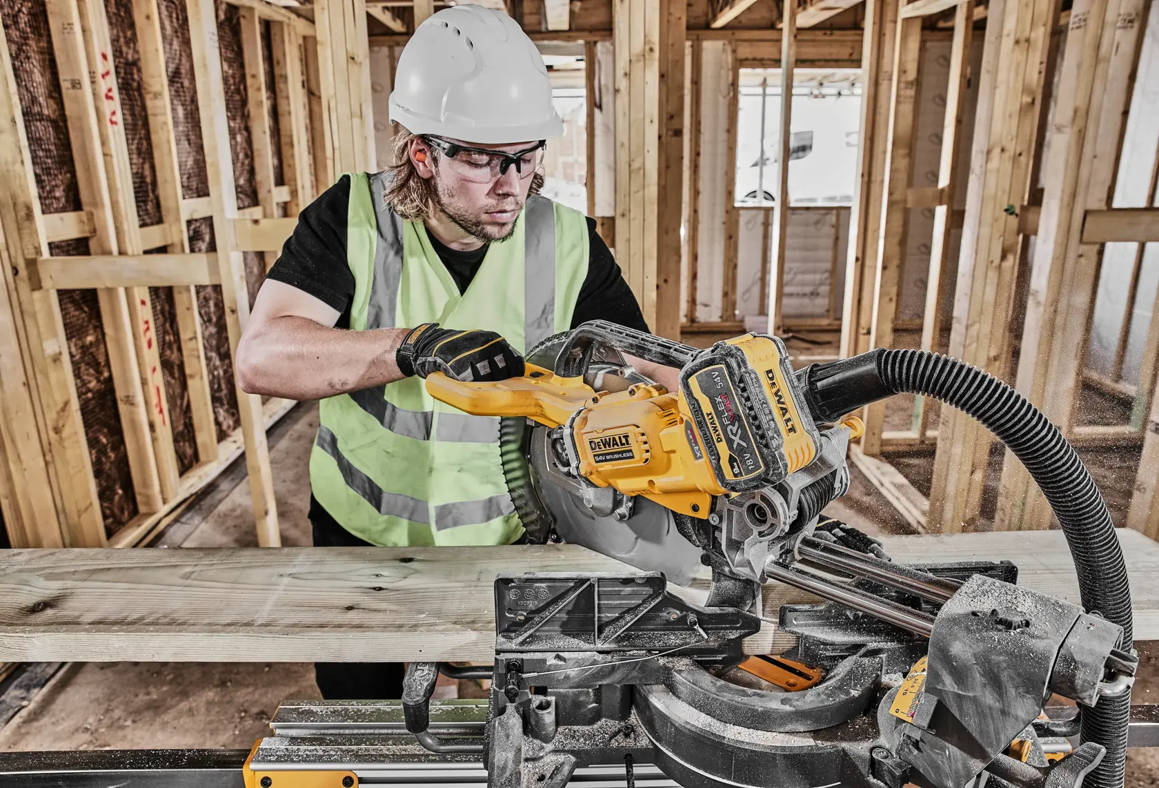 Arbeiter sägt Holz mit einer DEWALT DCS781N Säge auf Baustelle und trägt Sicherheitsausrüstung.